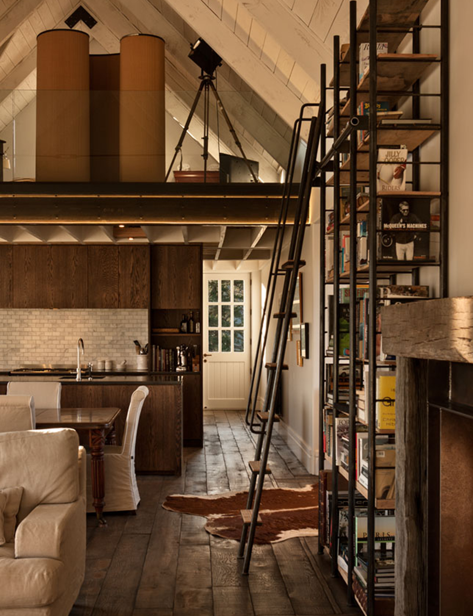 This barn-style interior of a Queenstown home by Bureaux has been mirrored in the steel tube and timber bookcase with library ladder. Image: Simon Devitt