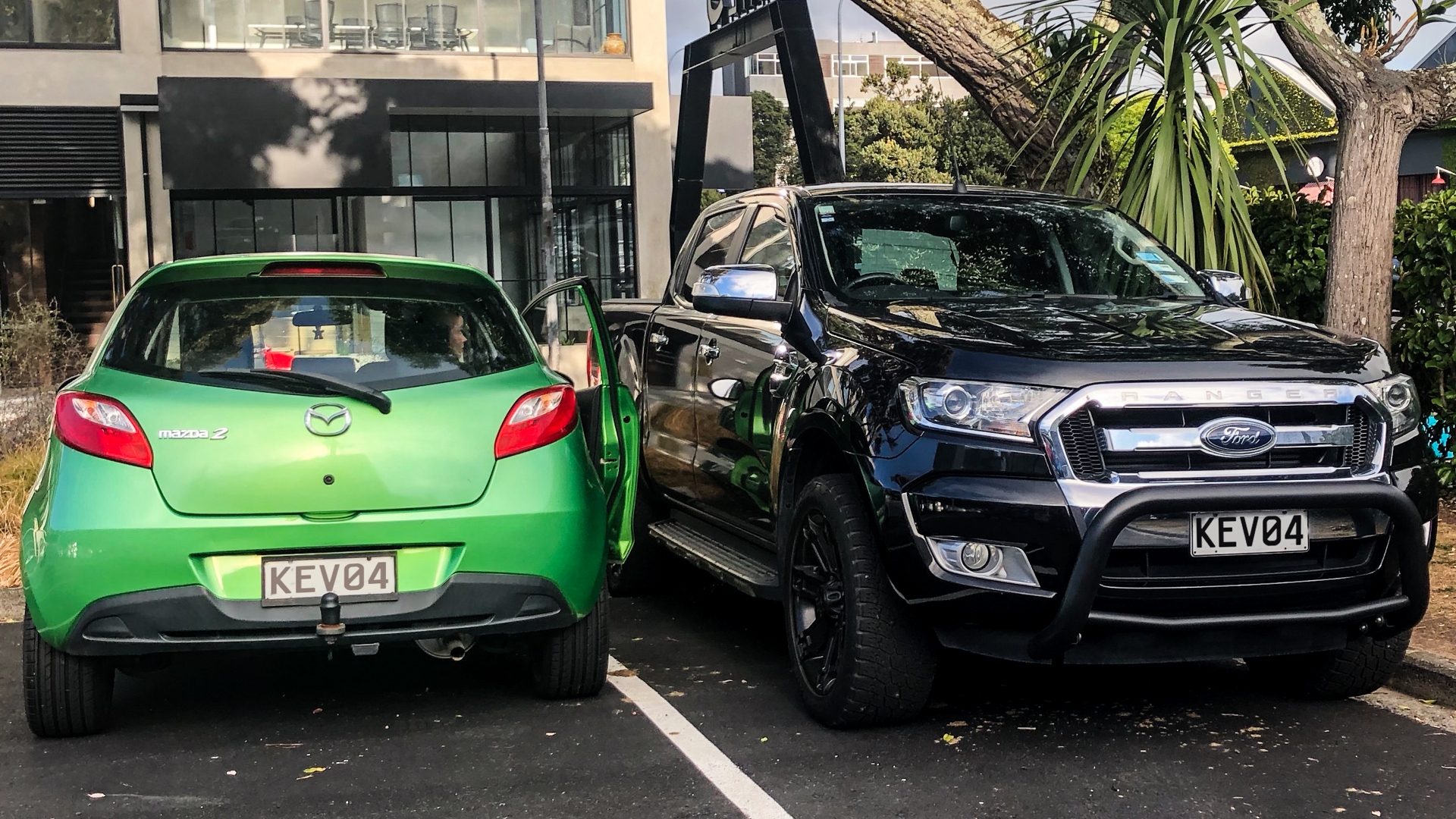 Little green car parked next to large vehicle