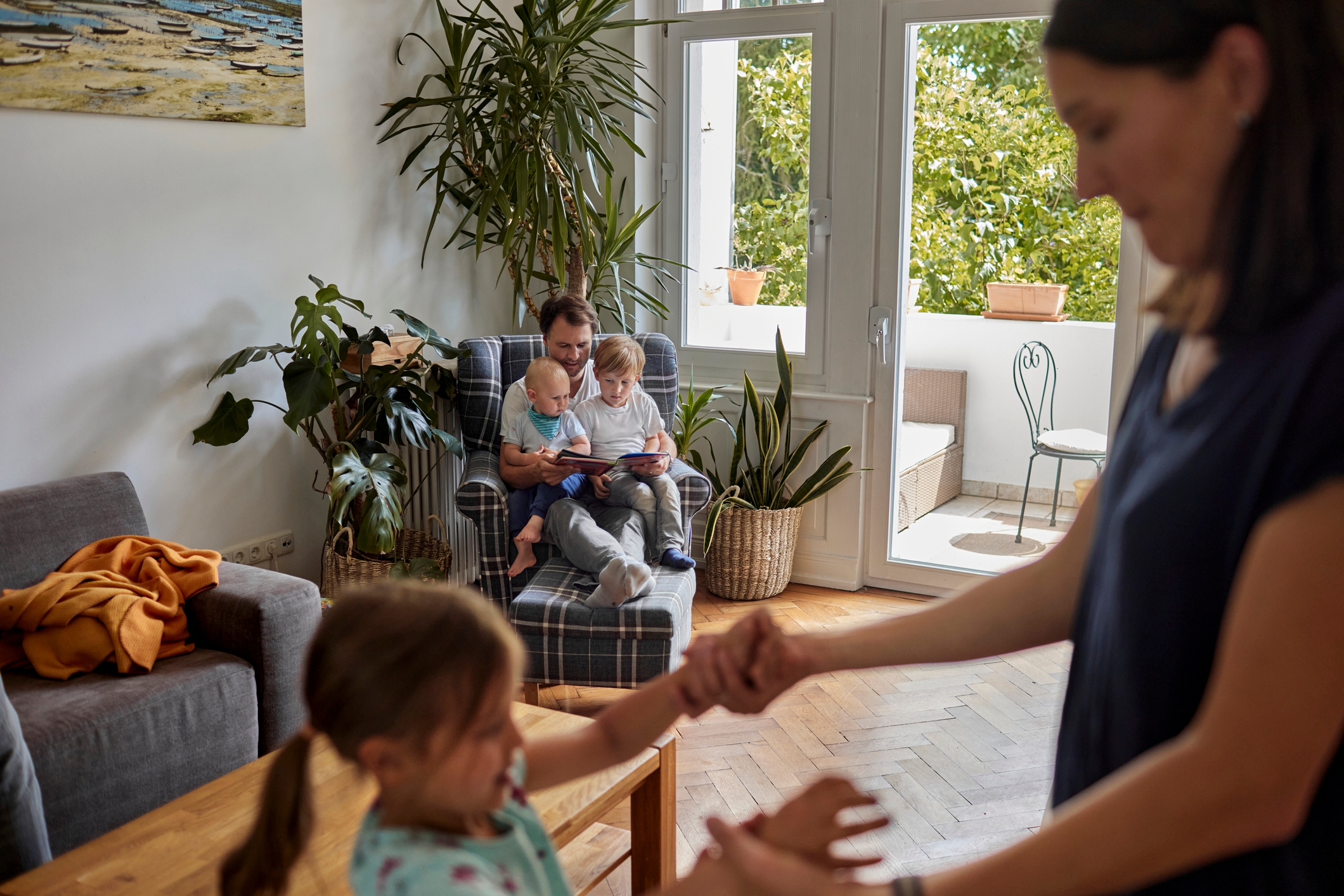 Mum and Dad at home keeping three little children occupied by reading and playing with them.