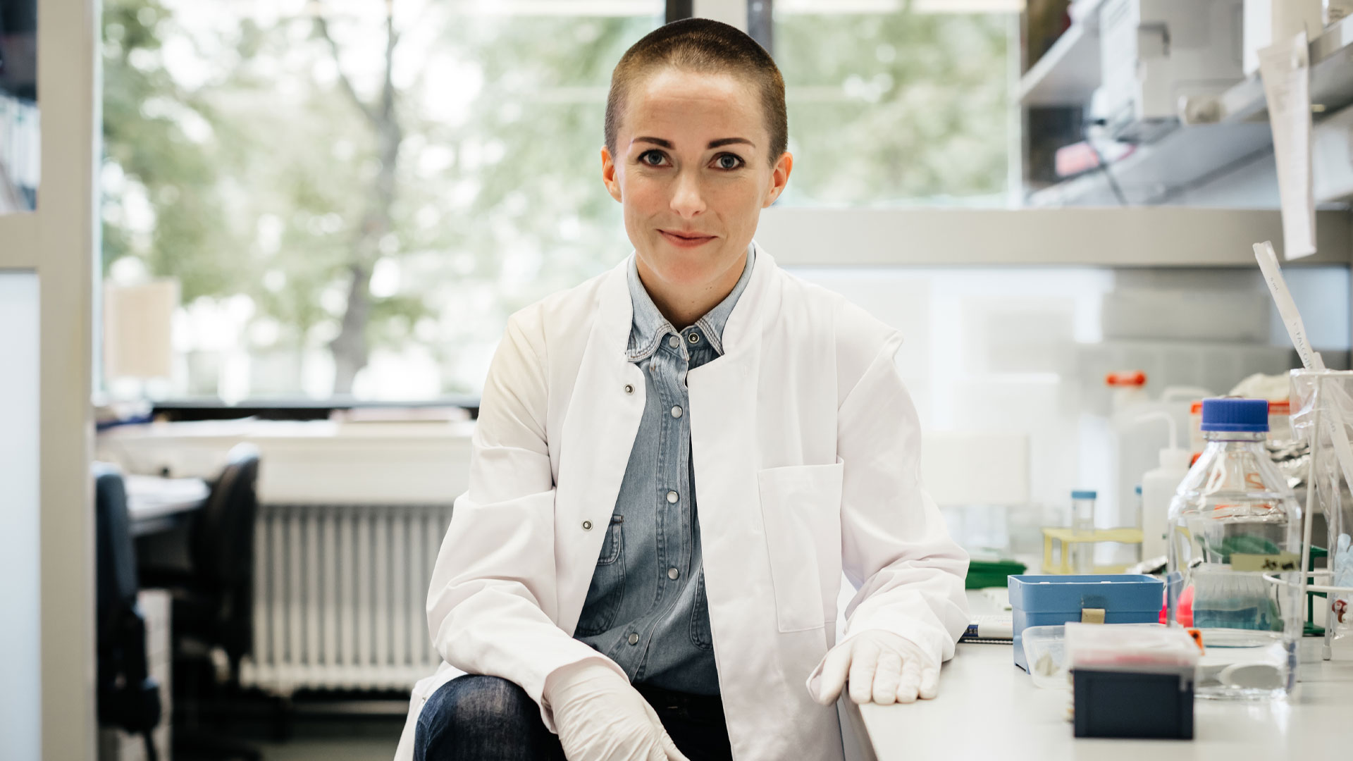 Young female scientist sitting in a laboratory wearing a white lab coat.