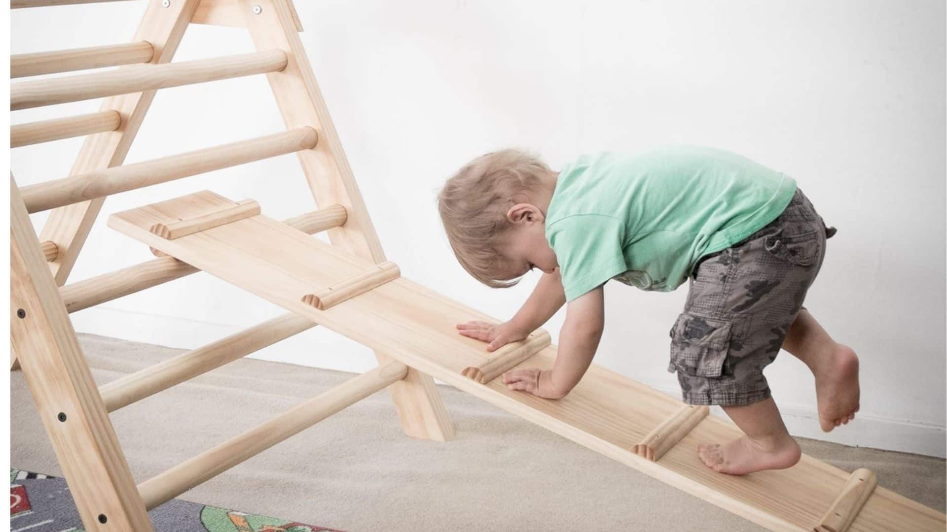 A small child climbs up a ramp leading to a pikler triangle.