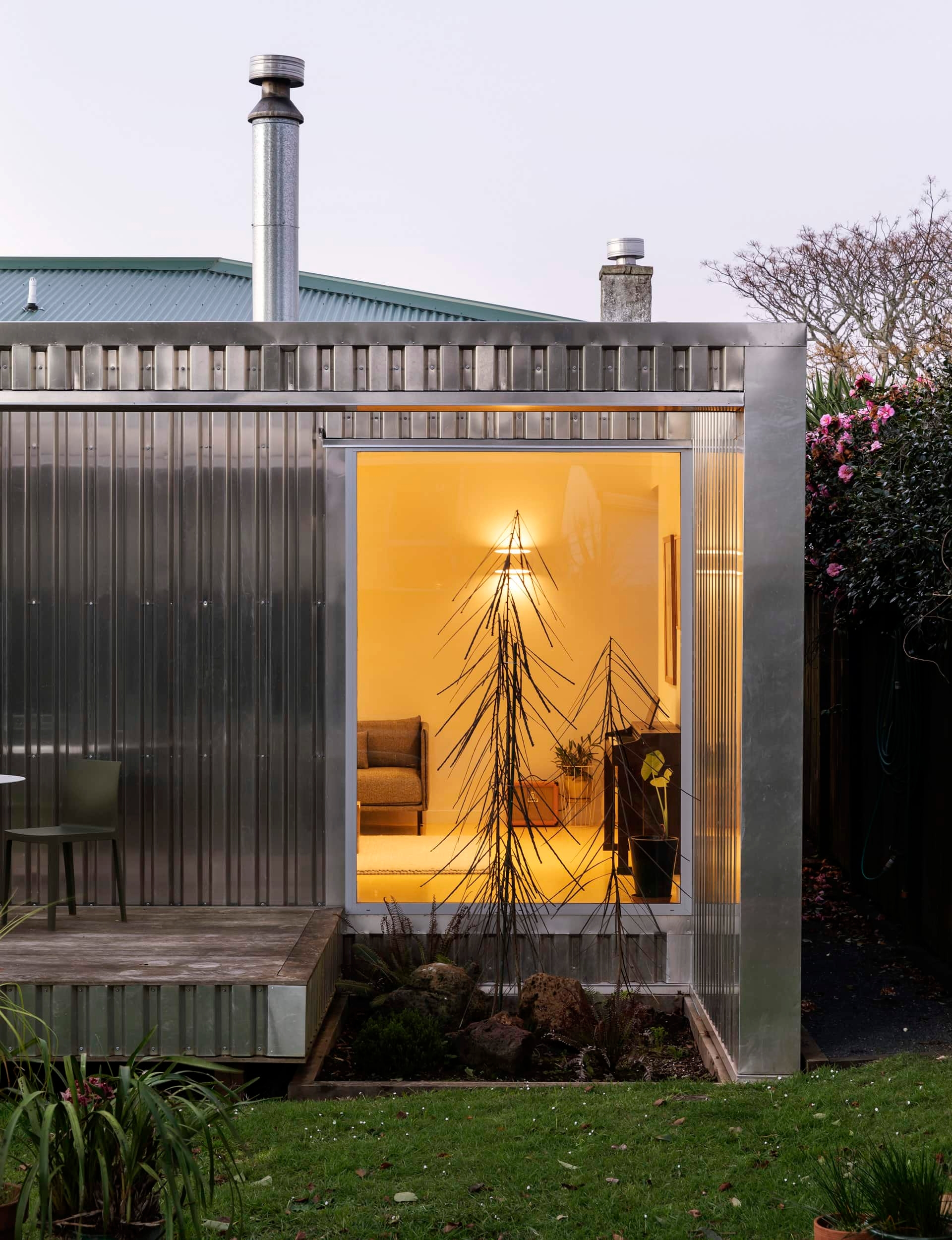 Small view into an illuminated living room with yellow floors through a tall window in front of a small sunken garden