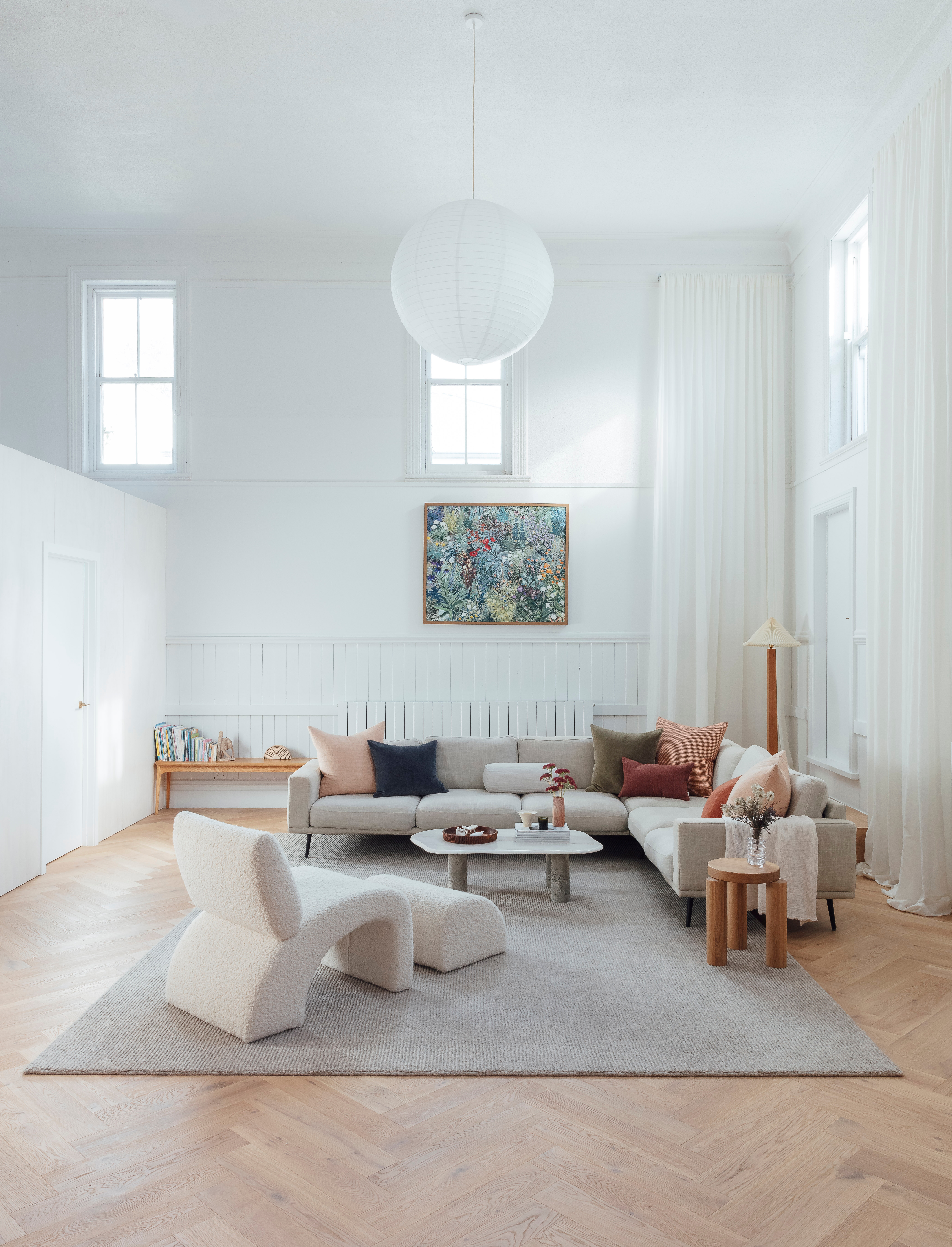 The addition of crisp, fresh white Dulux Ōkārito in the living space makes up for the lack of natural light. Also on the wall is a painting by Carmel Van Der Hoeven of George Sand Studio, which the couple commissioned. Curtains in Cavalier fabric from James Dunlop Textiles cascade from ceiling to floor, cushions from Città are dotted across a secondhand BoConcept sofa, and a custom rug by Nodi on the floor delineates this zone from the rest of the room. The coffee table was an upcycling project, and the vintage chair and ottoman were reupholstered in Fabio fabric from Warwick. The floor lamp in the far corner was handmade by Warren’s talented late mum, Yvonne; it’s recently been updated with a pleated shade.