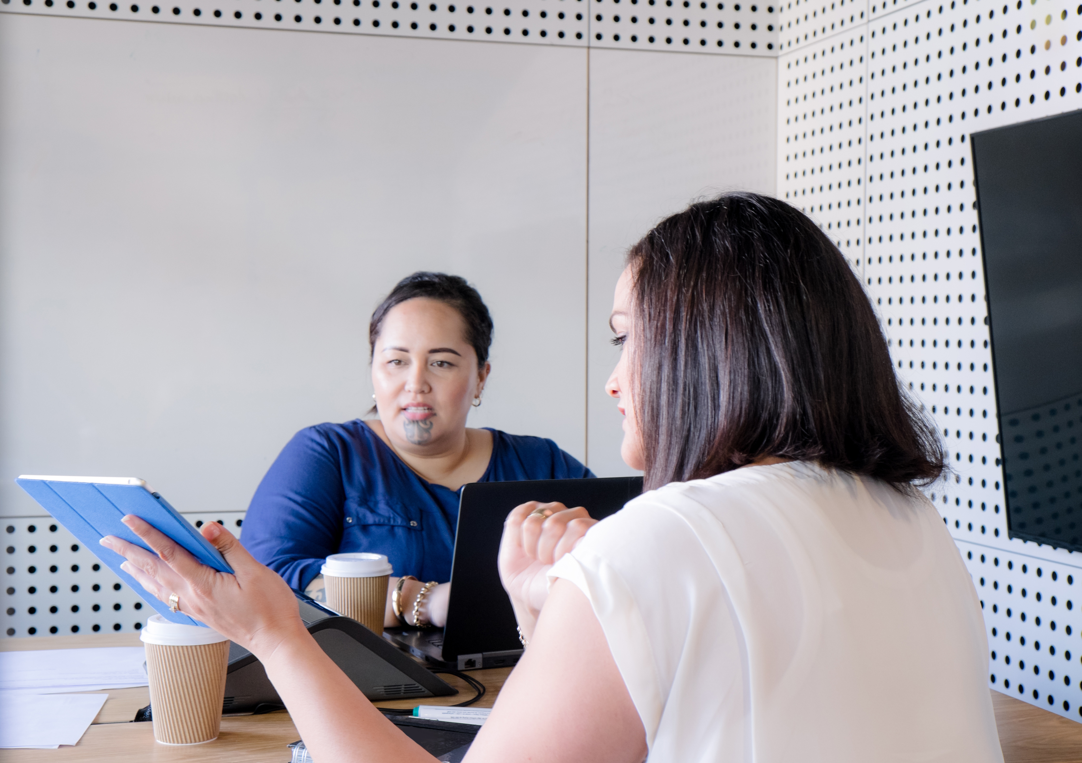 Two women sitting in an office space, looking at an iPad.