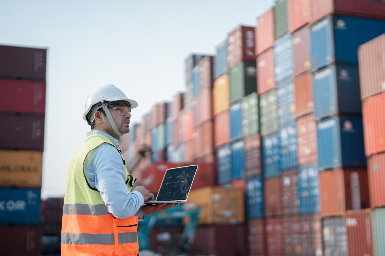 Man in hardhat and high vis vest looking at shipping containers. 