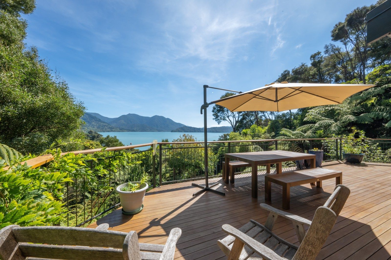 A house with a spacious deck overlooking calm water, with scenic mountain views in the background under a clear blue sky.