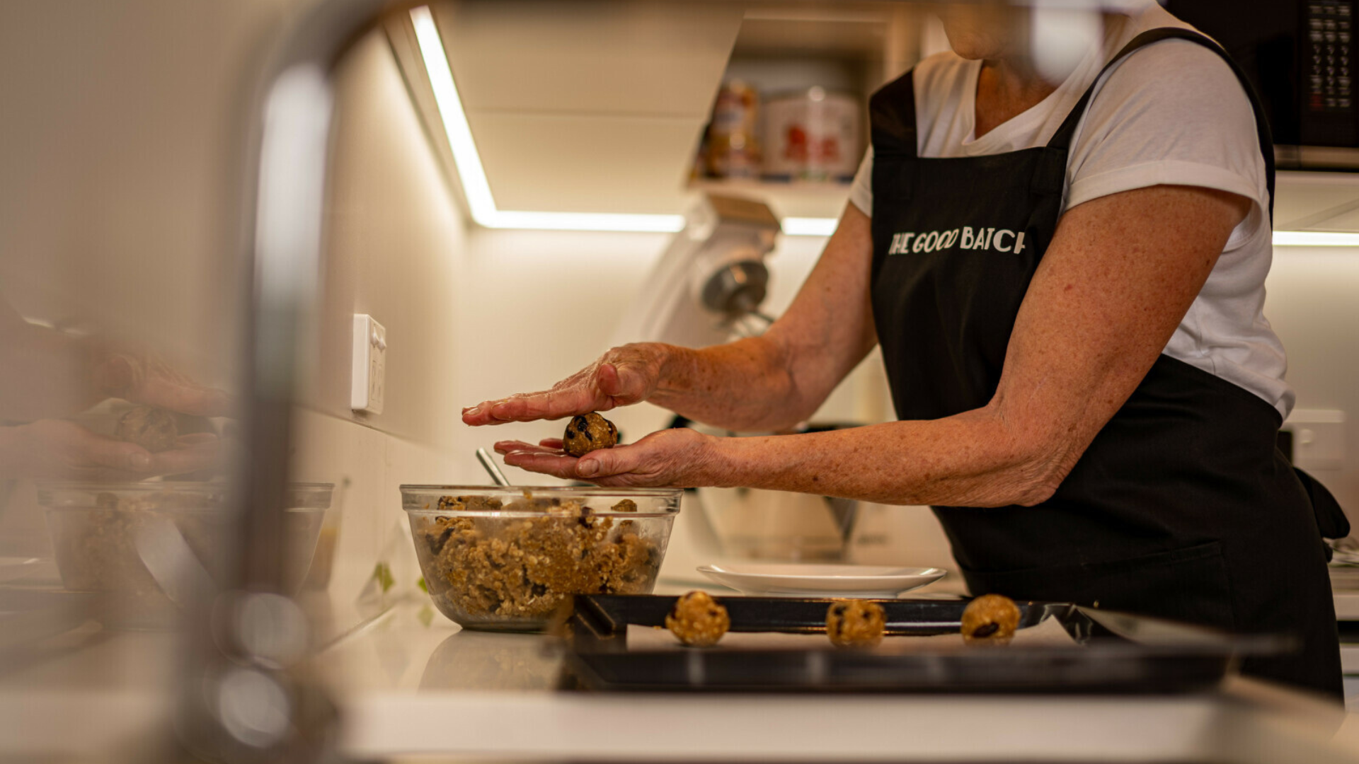 Woman in an apron rolling cookie dough into balls and putting them on a baking tray