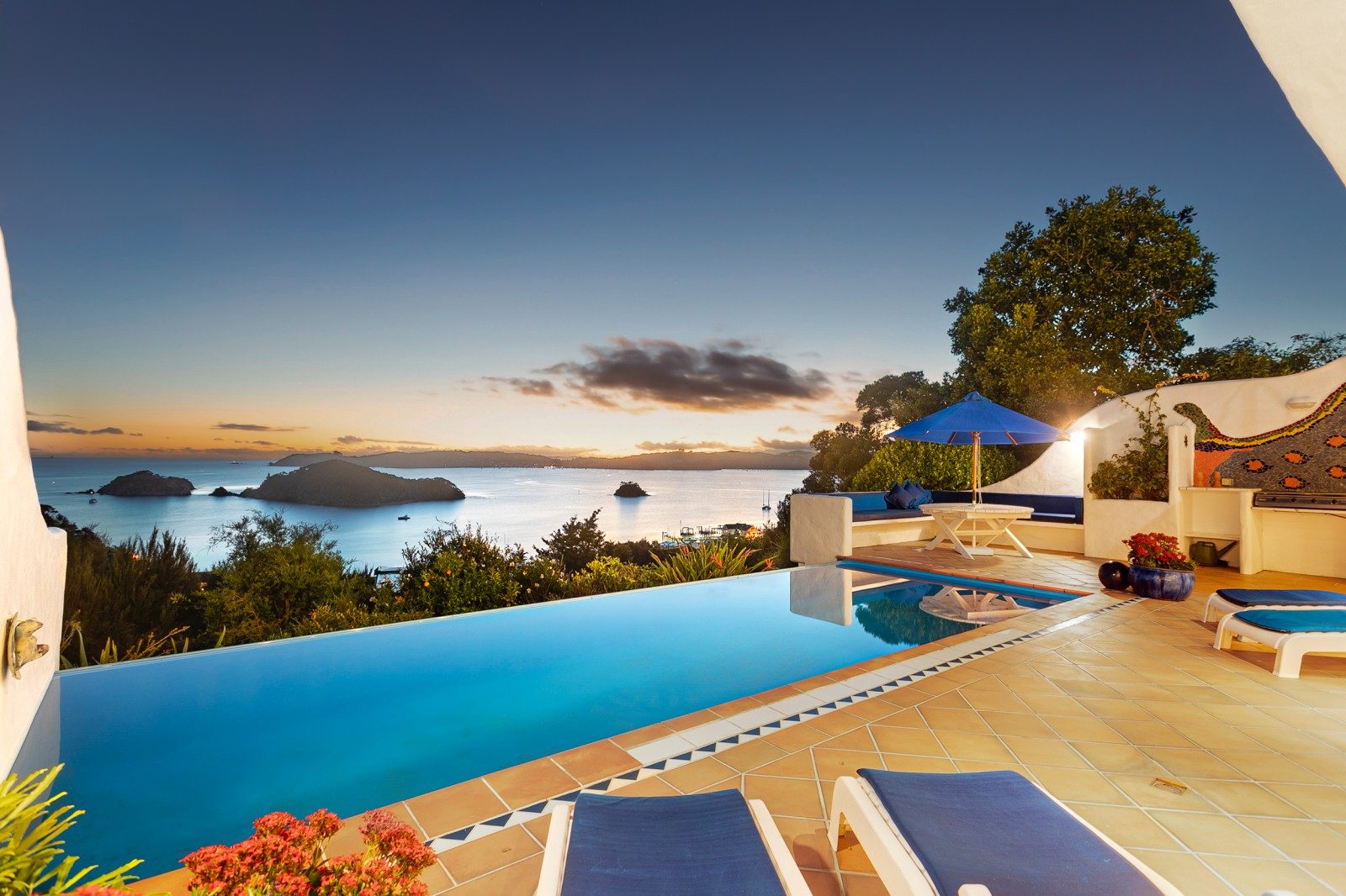 A large infinity pool looks out onto the Bay of Islands as the sun begins to set in the background.