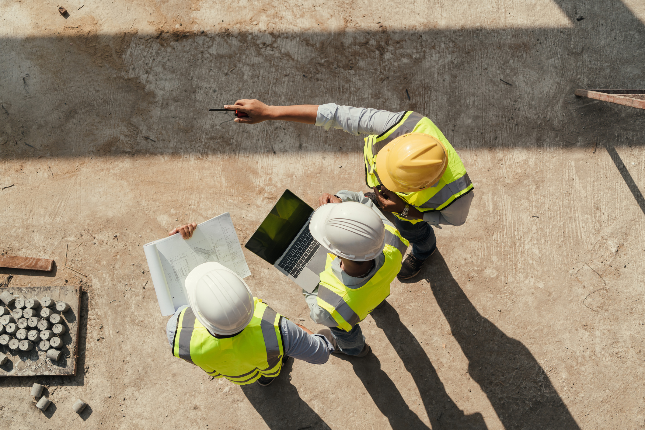 3 engineers looking at a laptop and standing on a building site