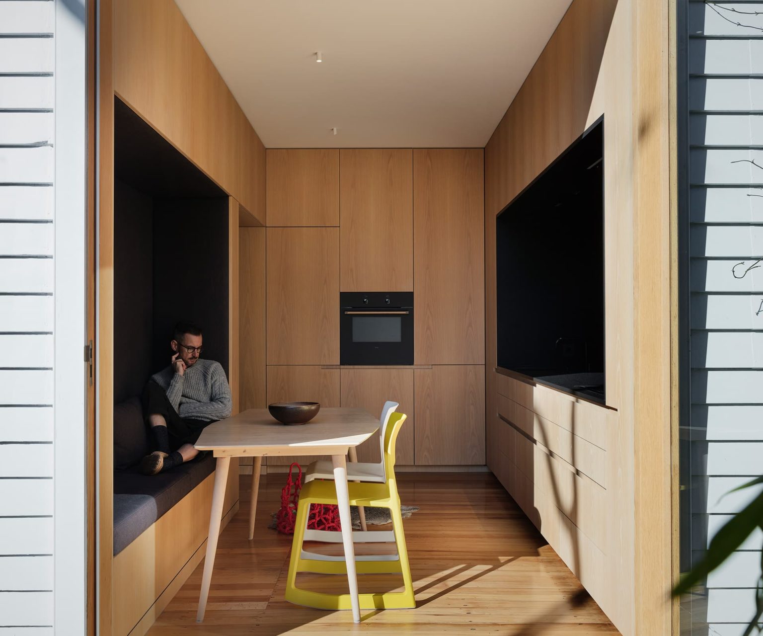 Small space with a wooden kitchen, bright coloured chairs with soft bench