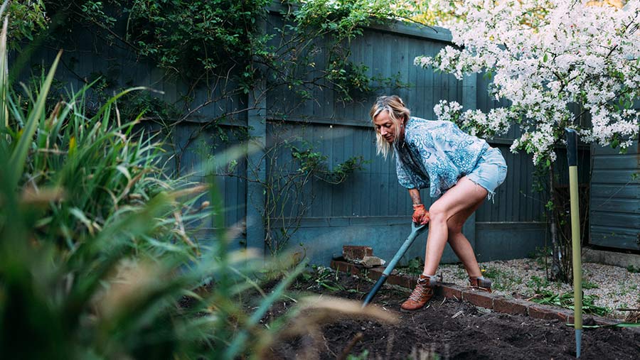Woman digging the soil in her garden to make it ready for planting.