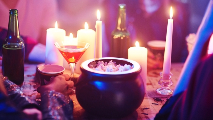 A table with candles, beer bottles, cocktail glasses and a miniature cauldron full of popcorn.