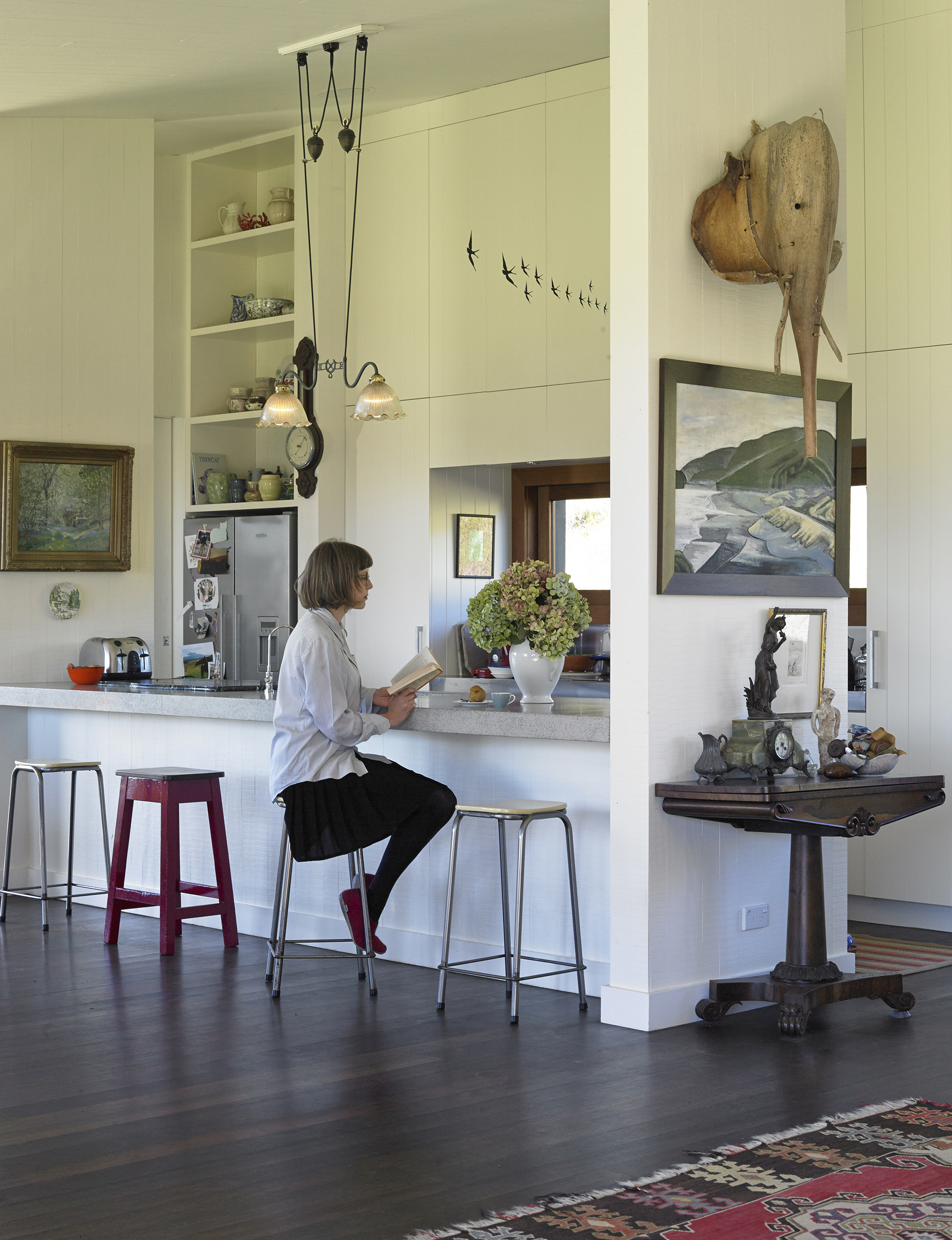 A woman sits at a white breakfast bar reading a book. 