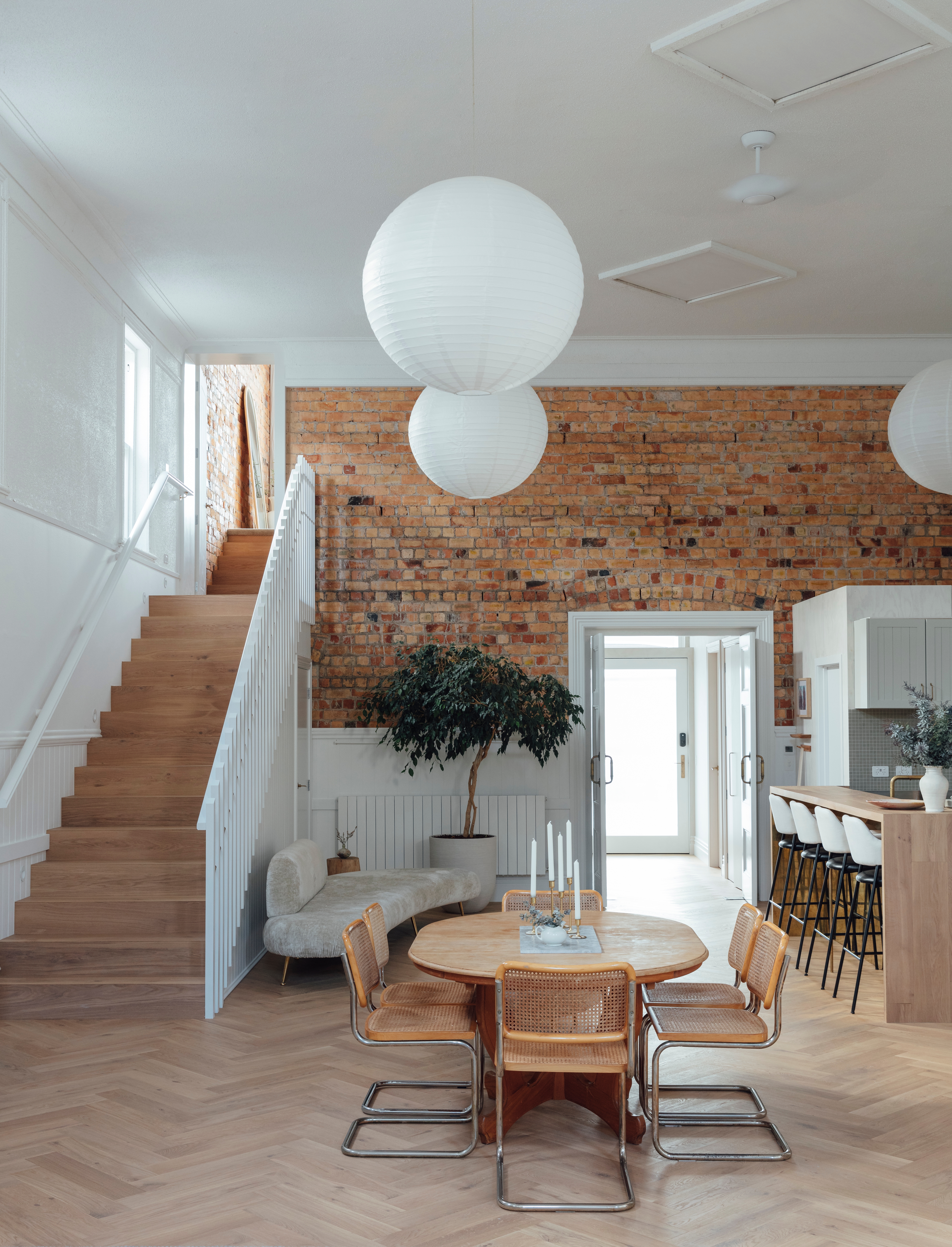 The front door ushers you into the lofty living zone in the hall proper, where oversized paper lightshades from Wah Lee are a practical way to fill the volume of the space. “They might be trending, but these lanterns are perfect here, as the ceiling is almost 6m high,” says Jess. Laid in a herringbone pattern underfoot, the Moda Capri planks from Forté Flooring were an early selection made in response to the soft terracotta hues of the hall’s original bricks. The dining table is a family heirloom, the chairs were bought secondhand and the bar stools were customised by Jess with new upholstery.