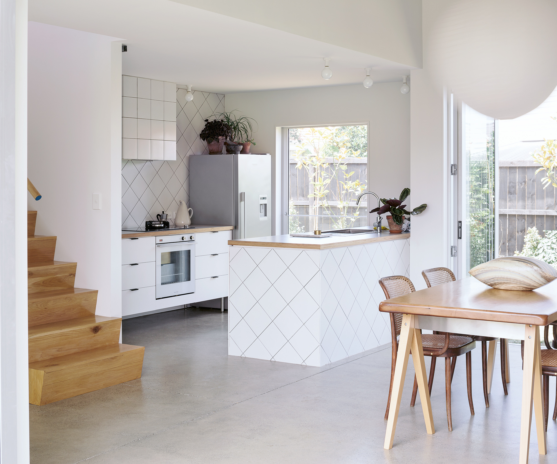 White bright kitchen with elements of wood added with the kitchen top, stairs and table combining the space.