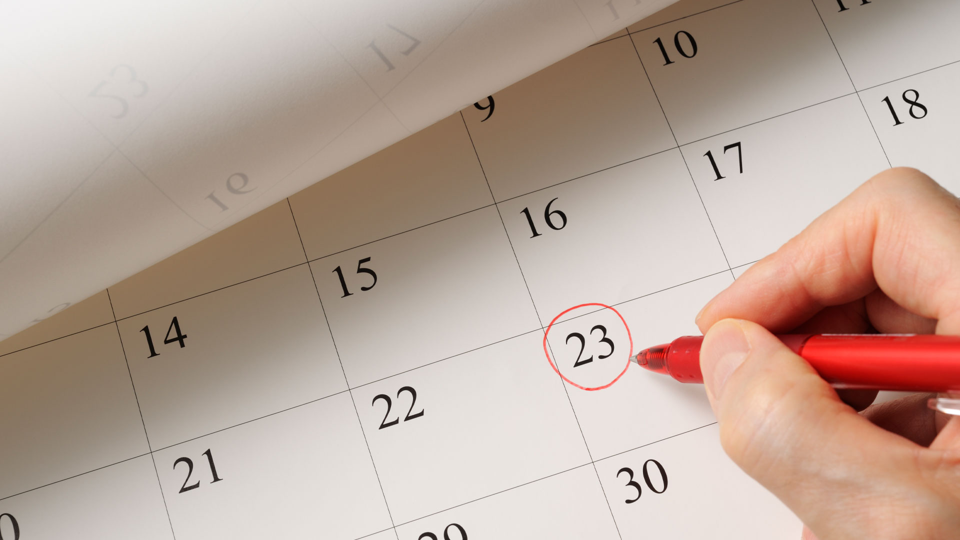 Person circling a date on a calendar in red pen.