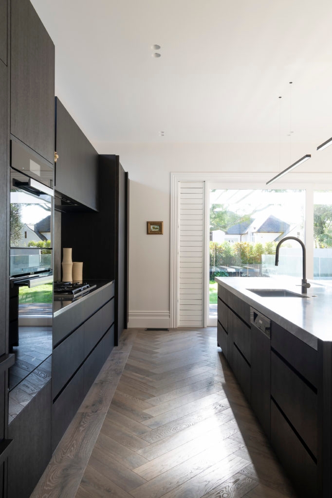 Portrait photo of galley kitchen, black cupboards and light wooden floors