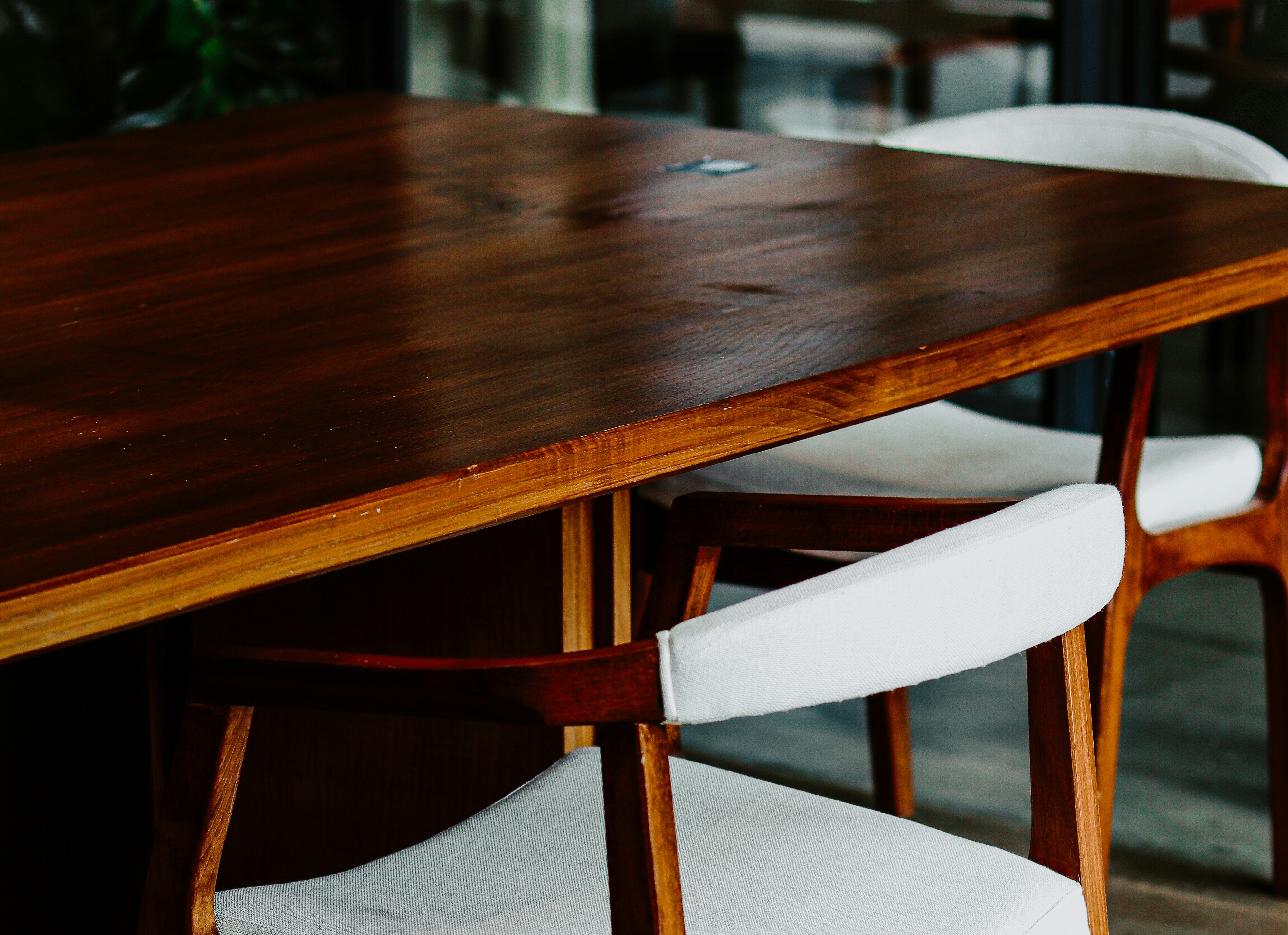 A wooden dining chair with a curved backrest and light grey upholstered seat, pulled up to a dark timber table.