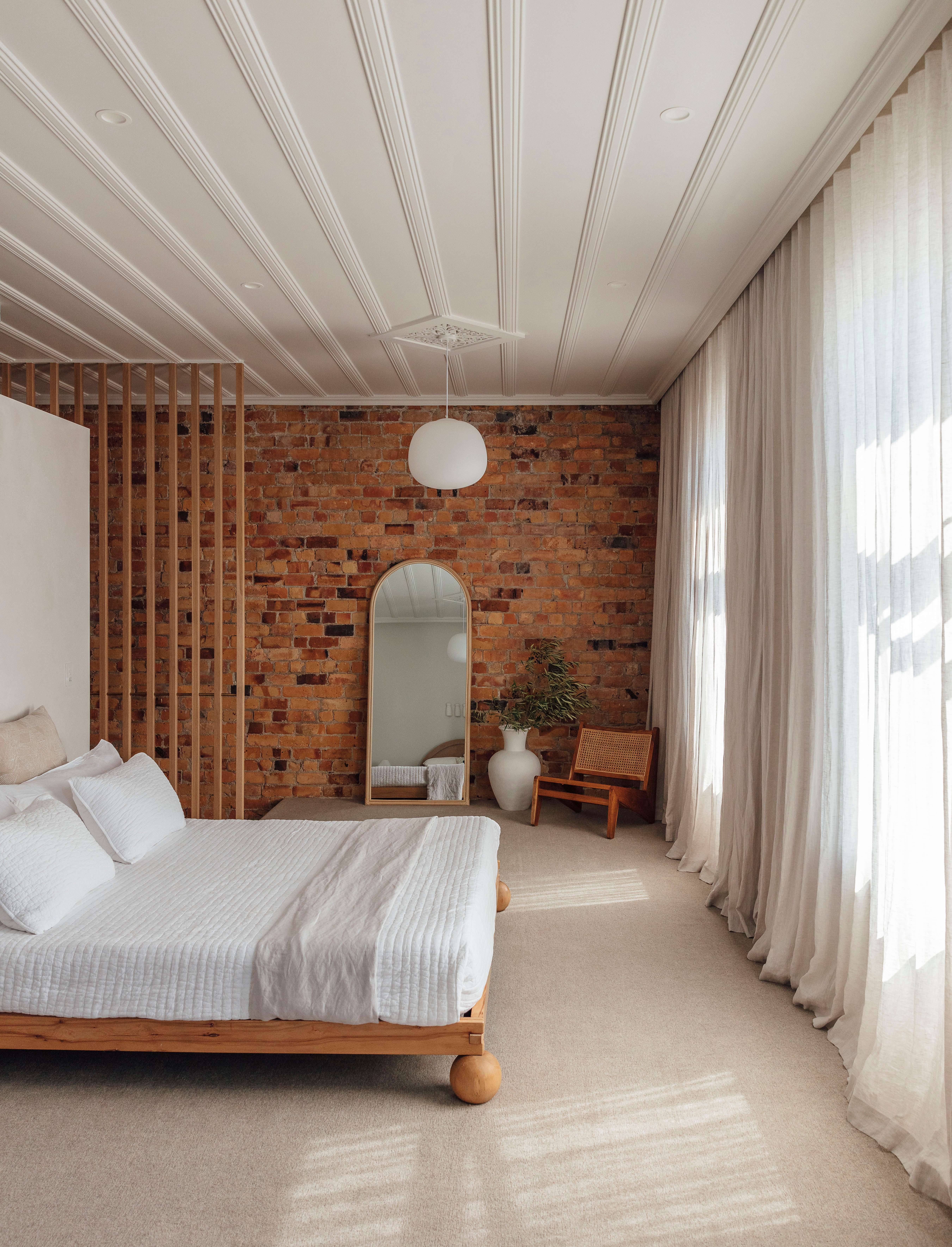 Pillowcases by Penny & Bennett and linen from Wallace Cotton dress the bed, another Trade Me score that was sanded back from black paint to natural wood. Kyoto linen curtains from James Dunlop Textiles filter the abundant sunlight that streams in through the sash windows. The Mary Arch mirror, large vessel and Hendrix chair are all from McMullin & Co, and the Ollie pendant light is from Mr Ralph.