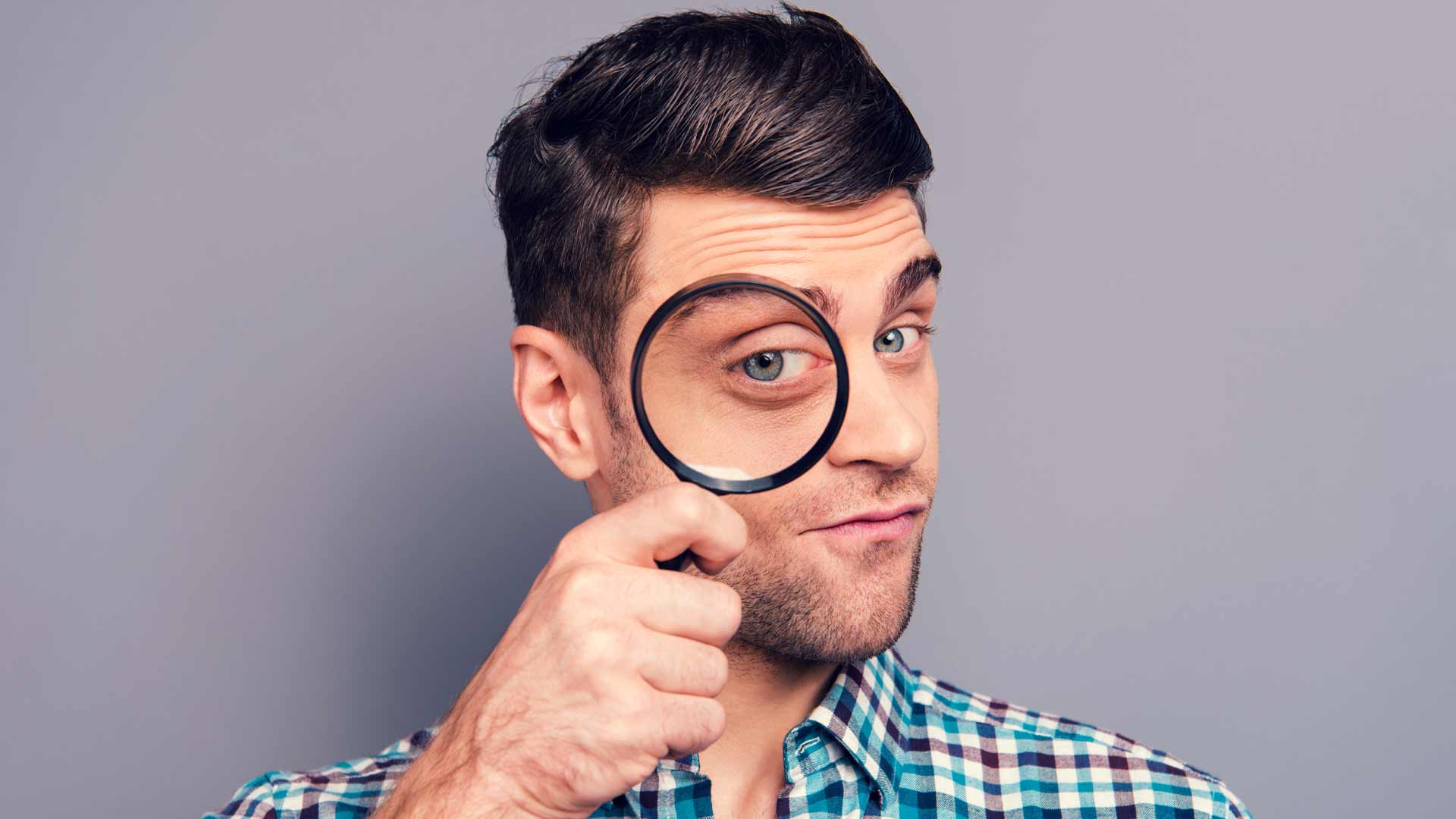 A man holding a magnifying glass up to his eye.