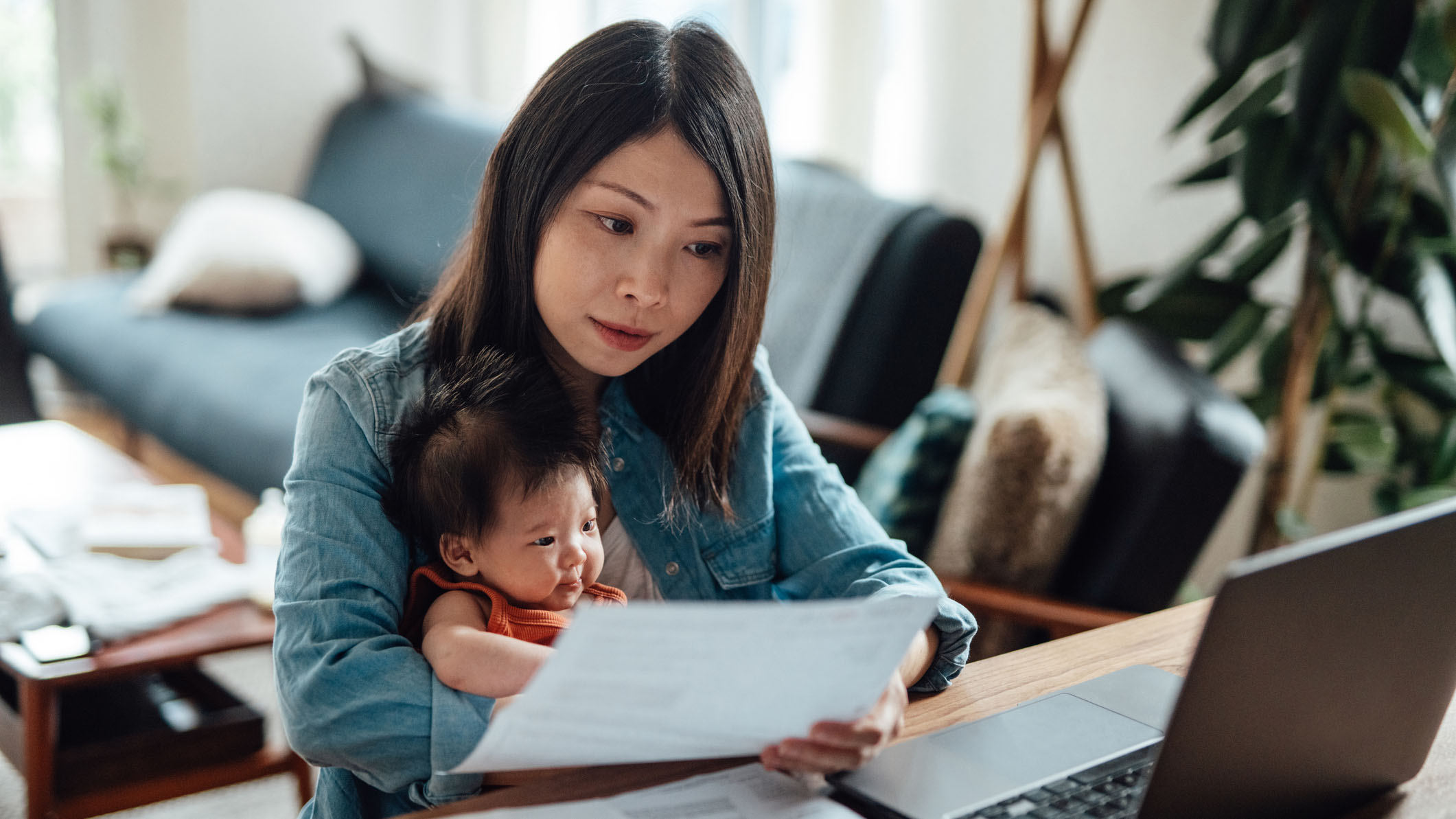 Woman with her baby checking her bank statements to review her spending habits.