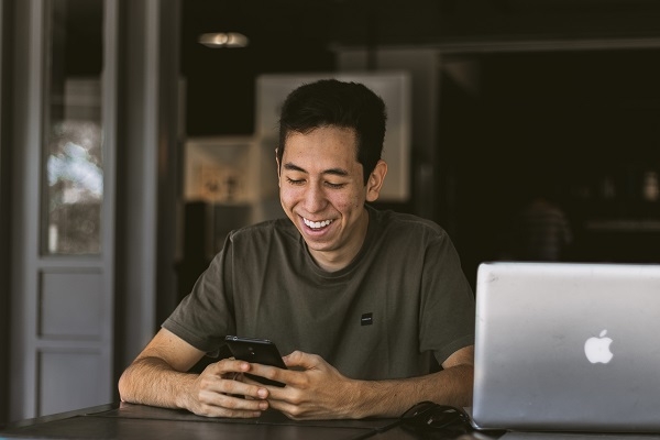 Man sitting a desk smiling at his phone as he corresponds with potential buyers for the items he’s selling on Trade Me.