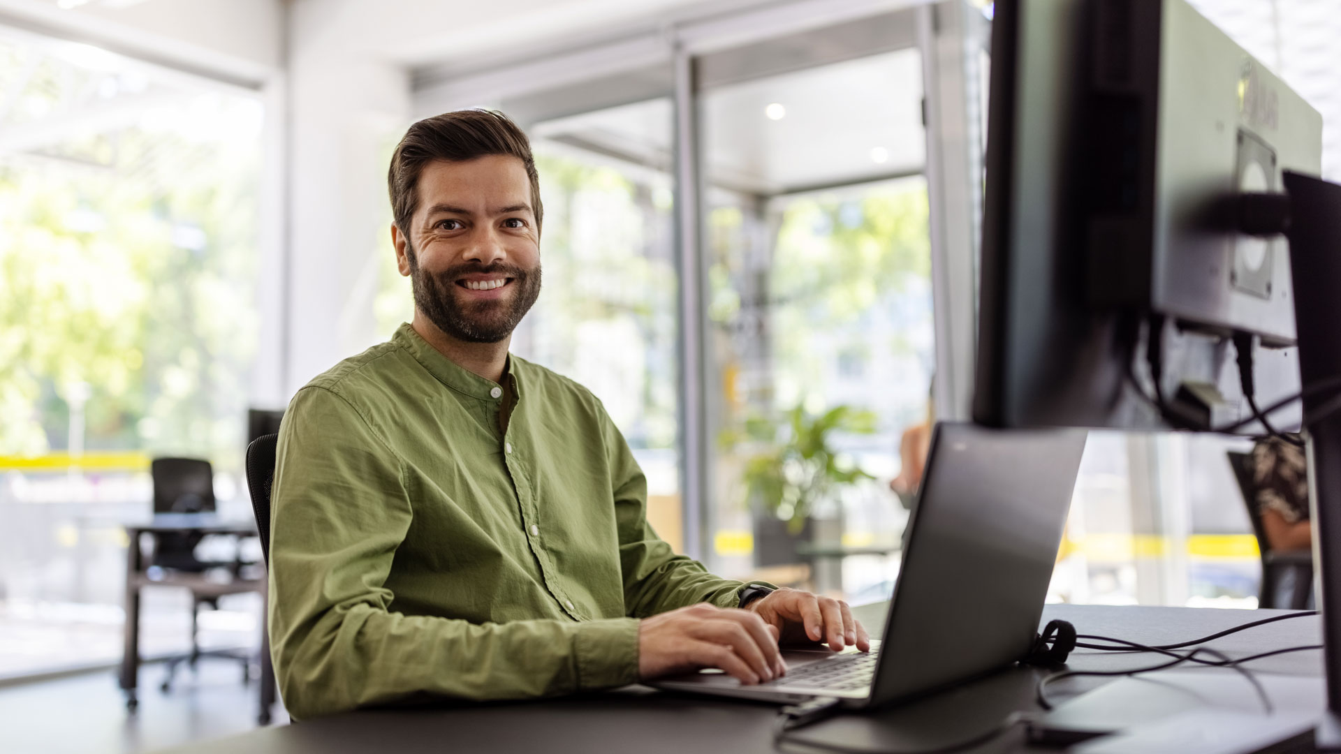 Man at work wearing a green shirt with his laptop smiling at the camera