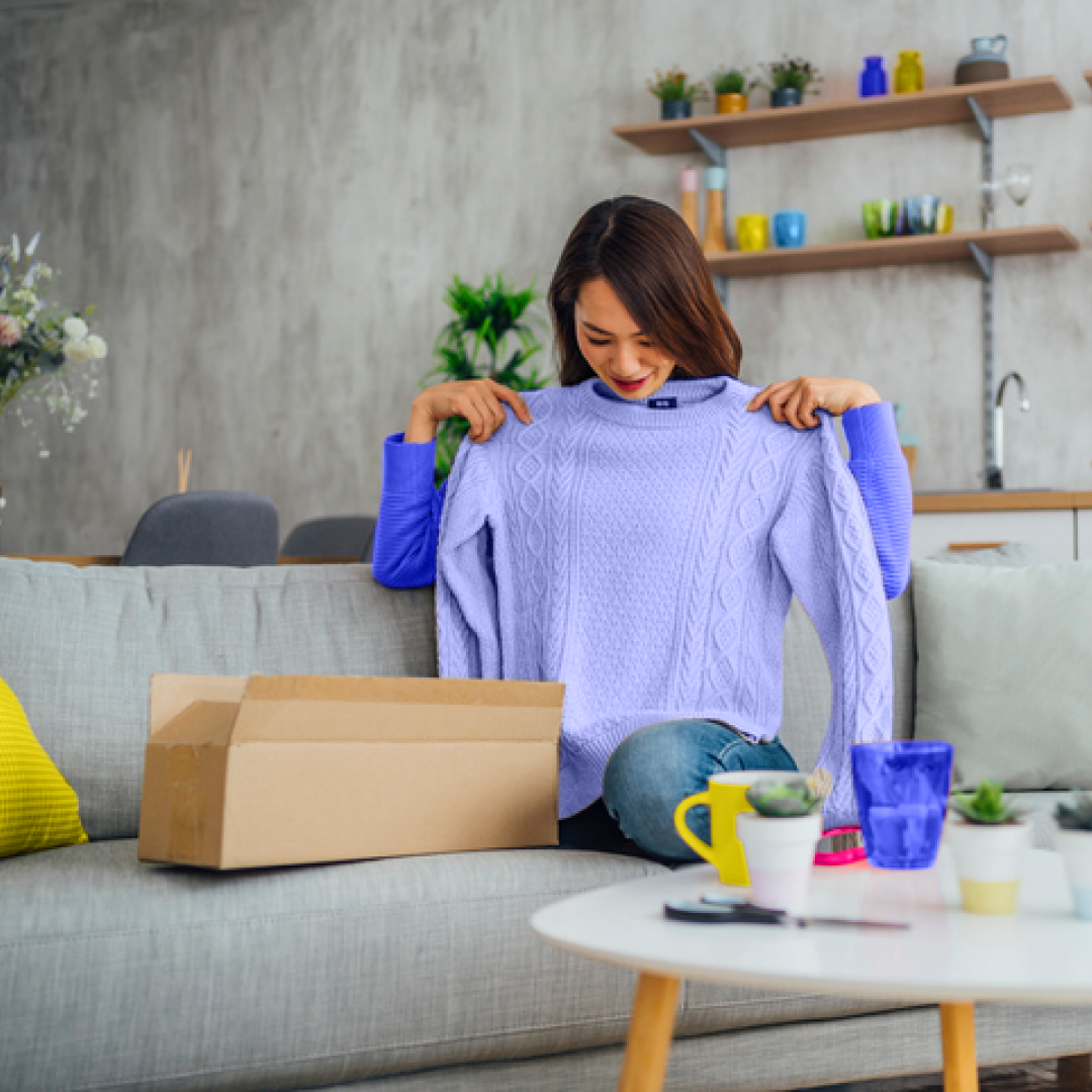 Woman holds up purple jumper to herself that she has taken out of a box