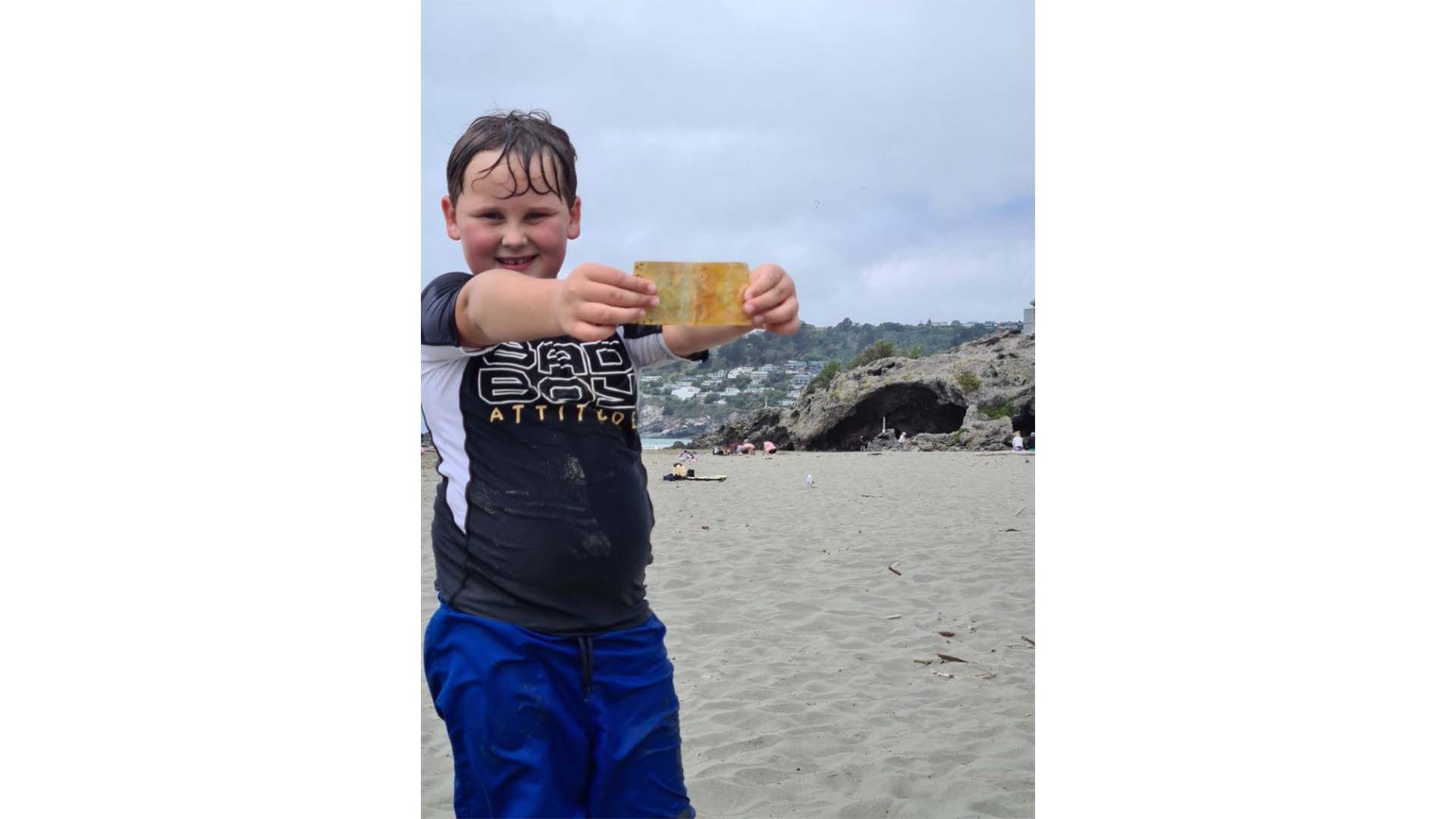 Zayne holding a $5 note discovered at Sumner Beach, sold on Trade Me for $1,000, supporting his dream.