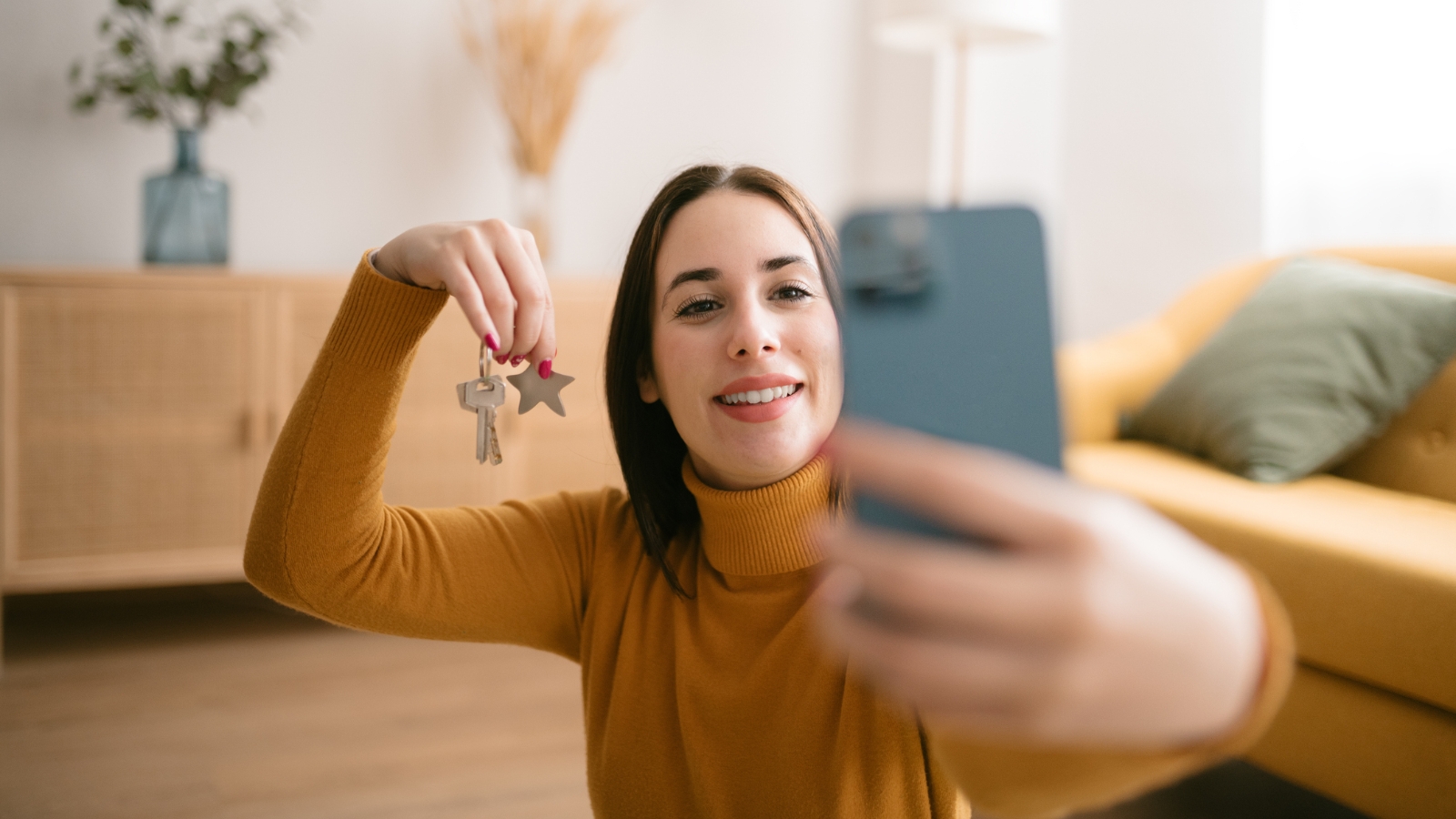 Lady holding up keys taking selfie in new home. 