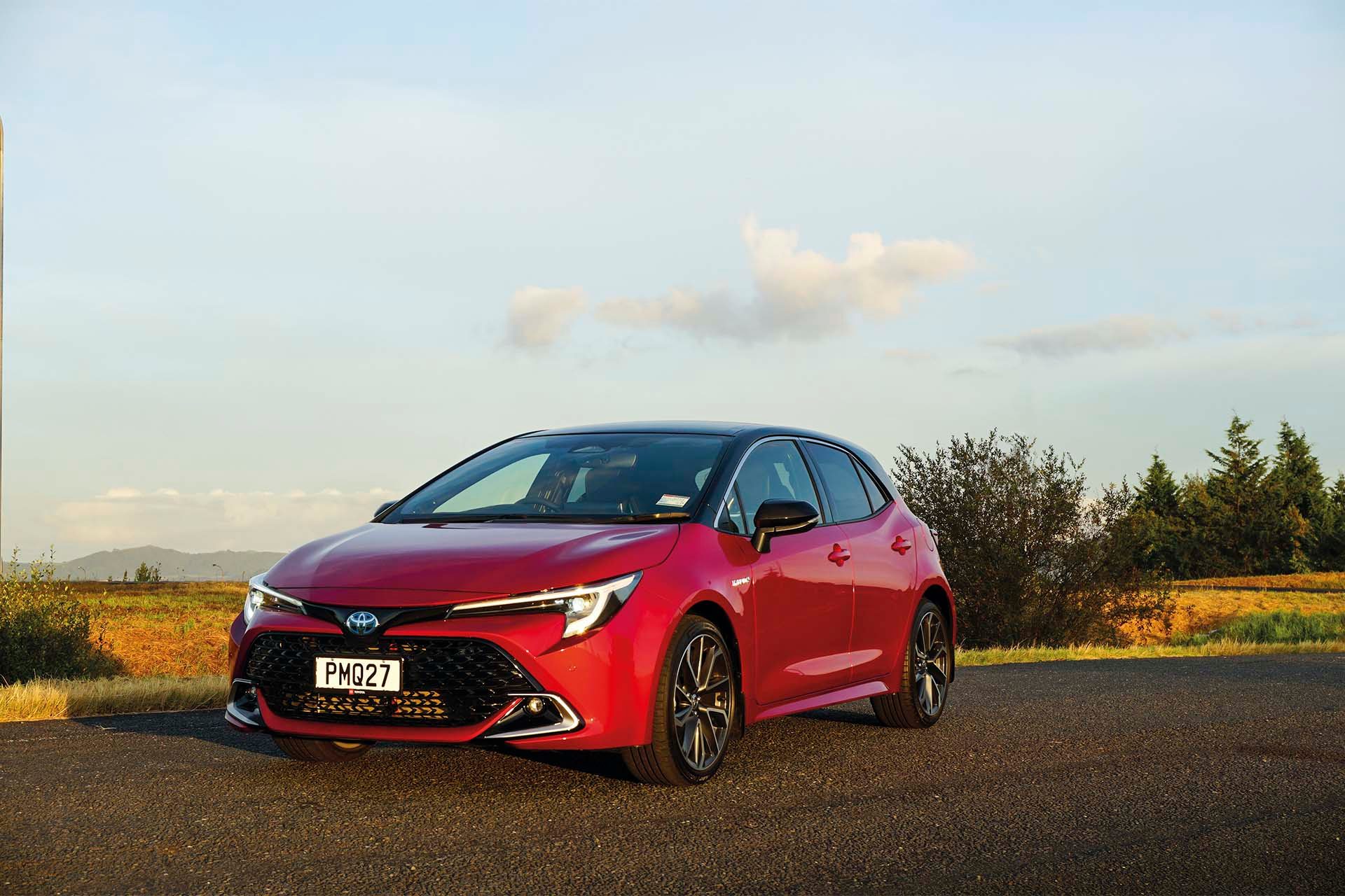 Red Hybrid Toyota Corolla front end stationary on road.