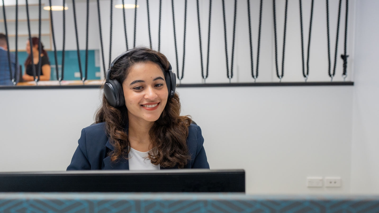 Lady in office in blue suit taking a call on a headset. 