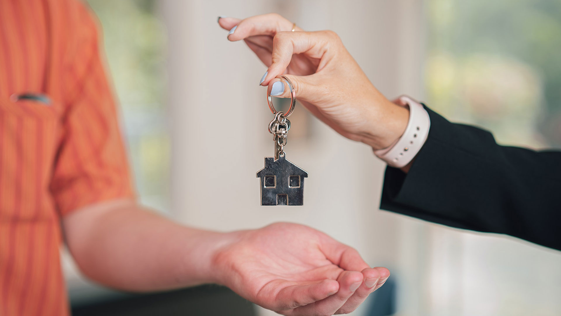 Real estate agent holding up a key ring with a home icon on it and passing it to the new homeowner.