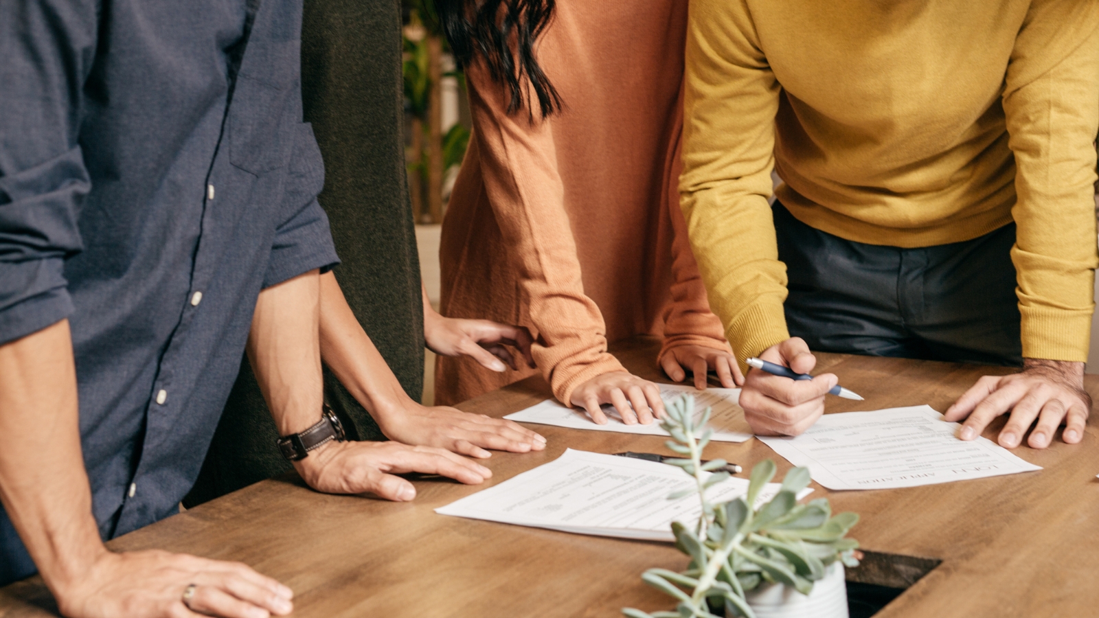 Multiple people standing at table signing document. 