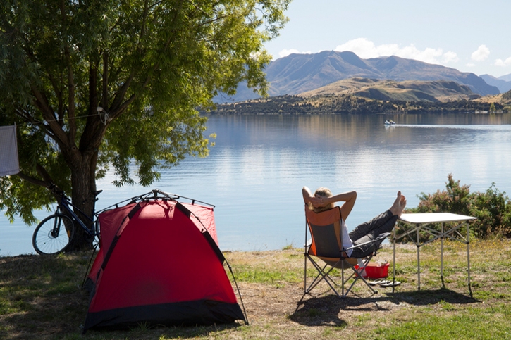 Woman relaxing at a lakeside campsite with her tent, camping chair and bike