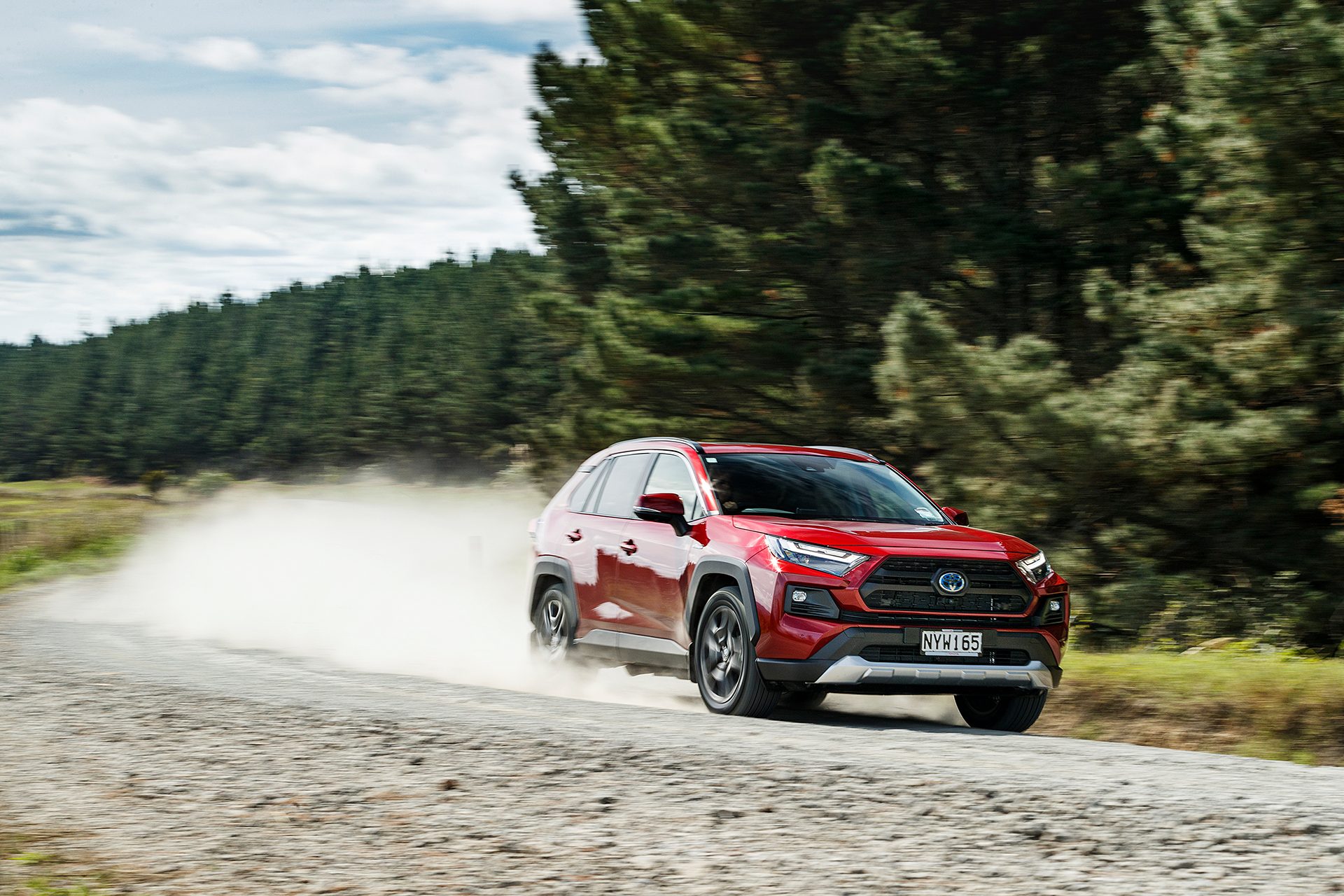 Red Toyota RAV4 Adventure Hybrid driving on gravel road front shot.