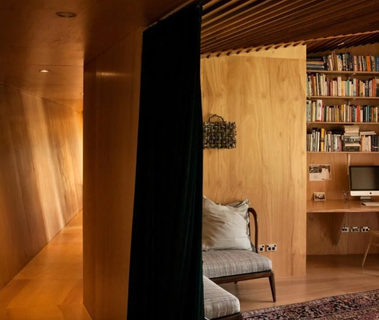 Wood-paneled room with a dark curtain acting as a divider, revealing a cozy reading area with a chair and bookshelf.