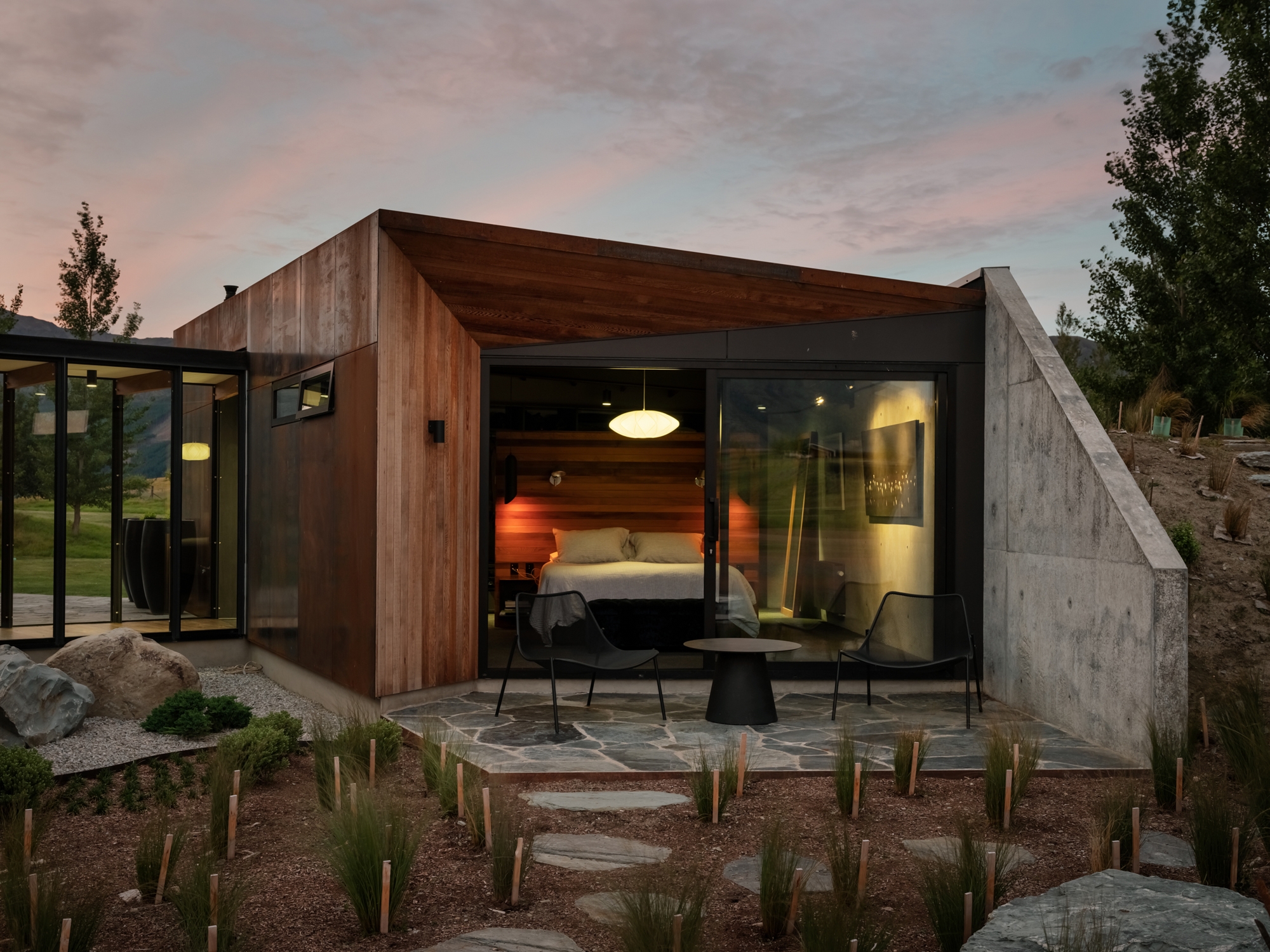 From the outside looking in, a bedroom with huge floor to ceiling doors that allow in lots of natural light and beautiful views. The tone inside the room is set with mood lighting which are soft and warm.