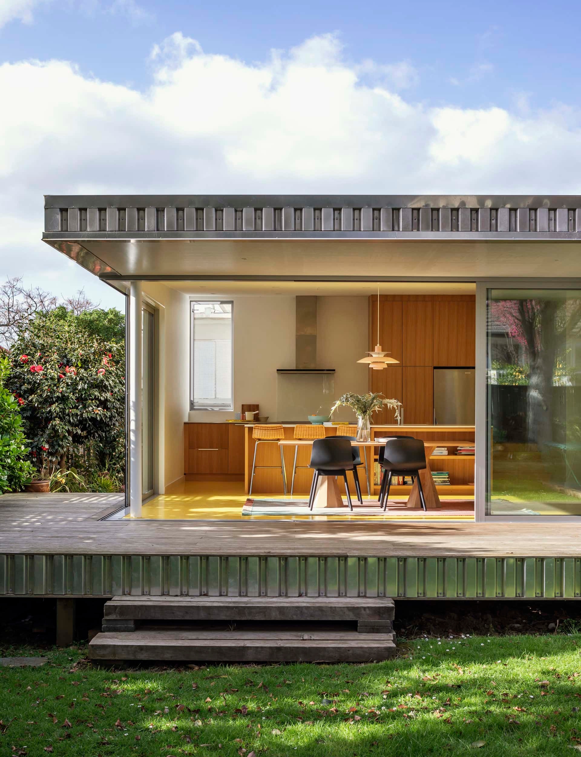 View from outside of a modern kitchen with yellow floors leading out to a wrap around deck 