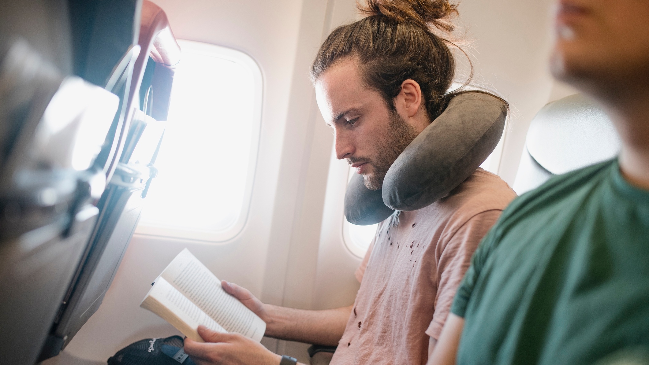Man reading on a flight wearing a neck pillow.