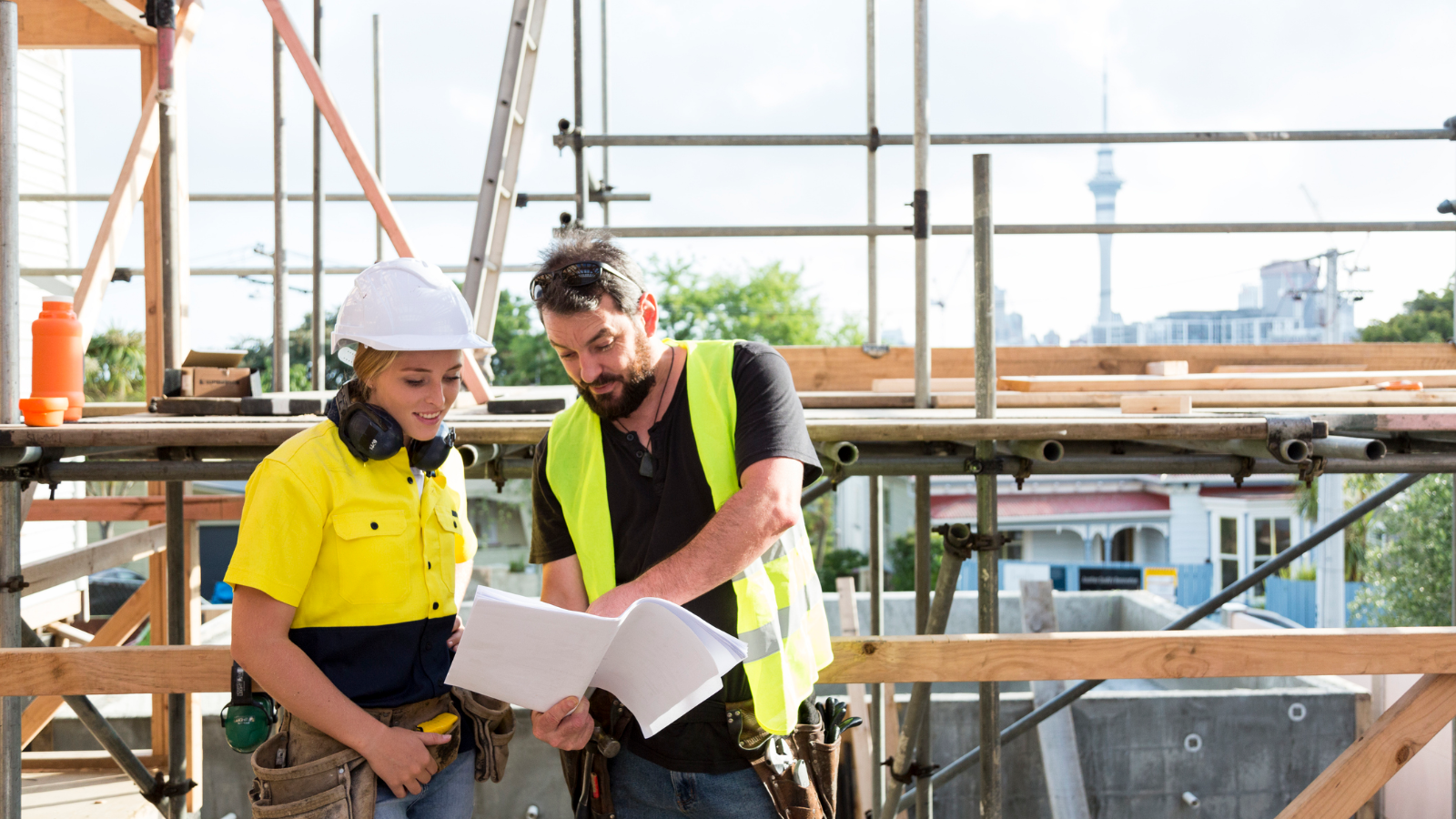 Man in high vis showing apprentice documents on building site. 