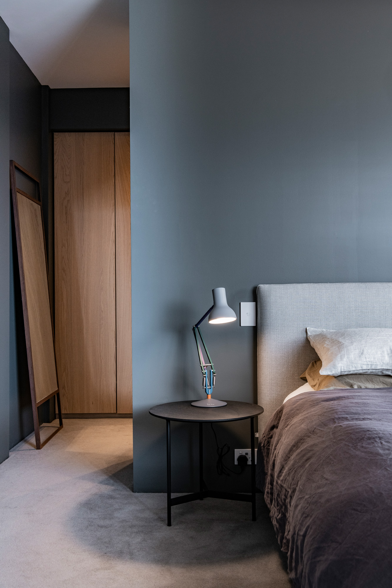 Bedroom corner with half of a bed in neutral resene grey tones, paired with a sleek bedside lamp, creating a calm and cozy atmosphere.