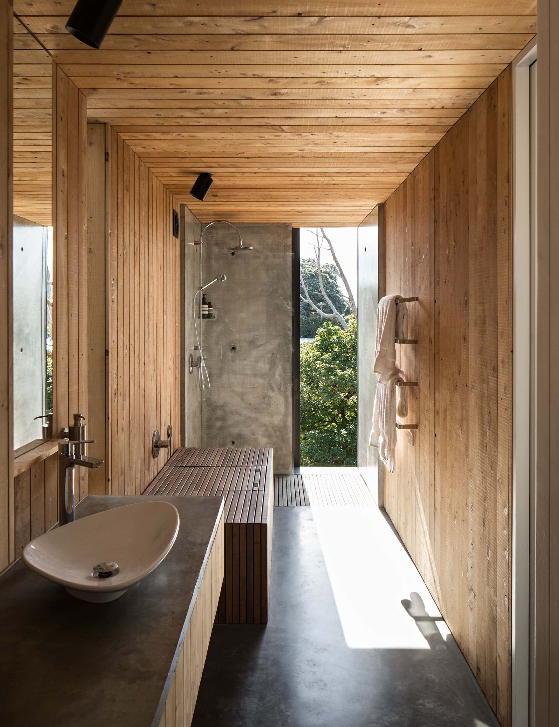 A serene bathroom featuring wooden paneling made from natural resources, offering a picturesque view of New Zealand bush through a large window.