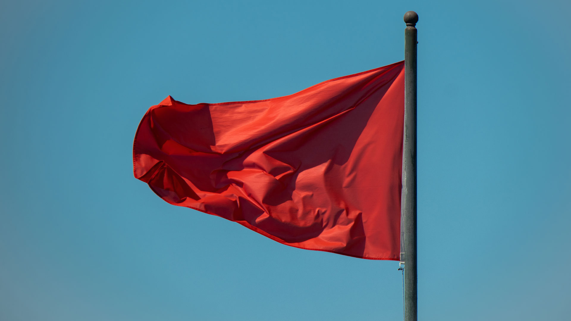 Red coloured flag blowing in the wind.