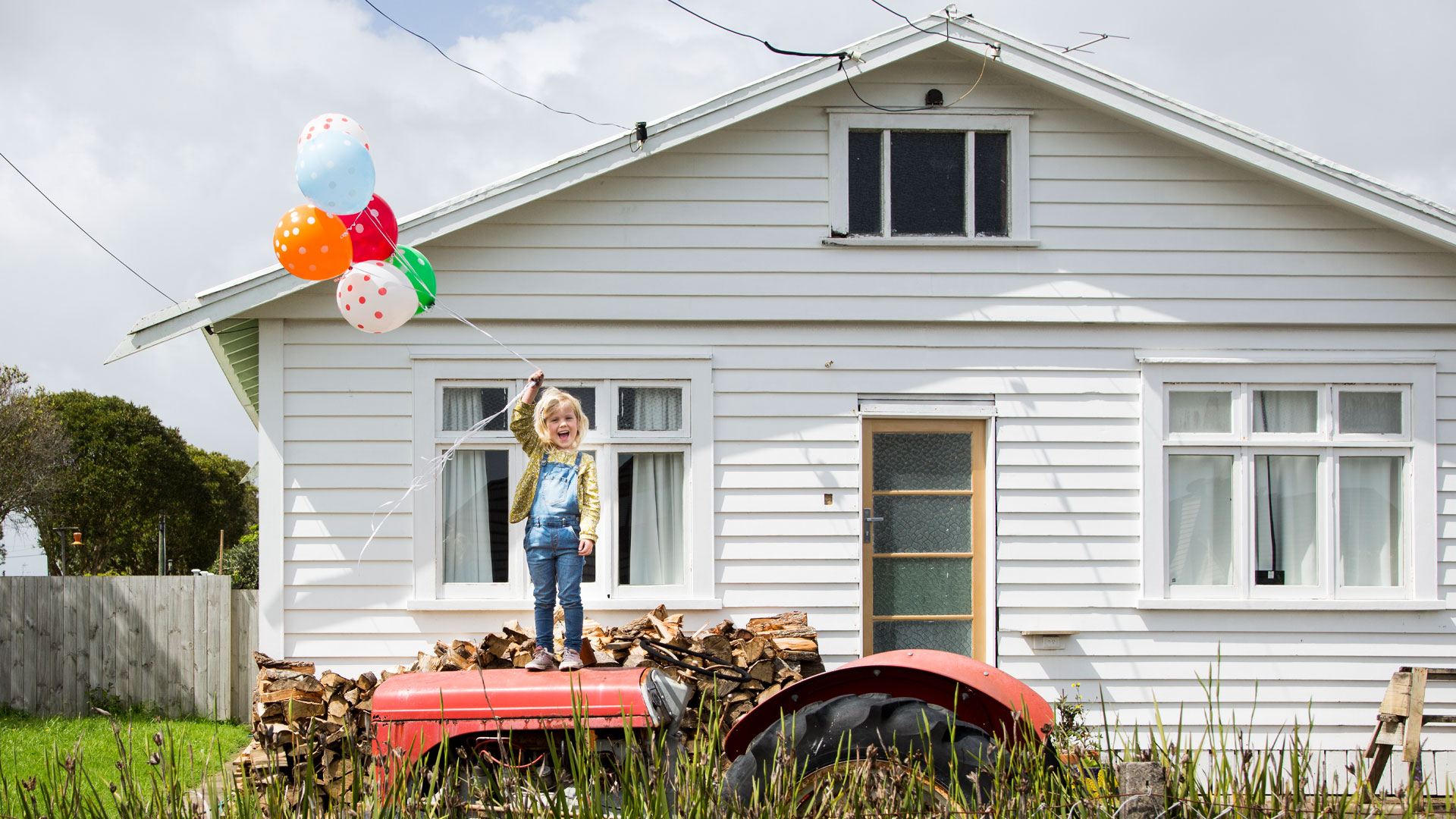 A girl with balloons standing on a tractor outside her home in Southland.