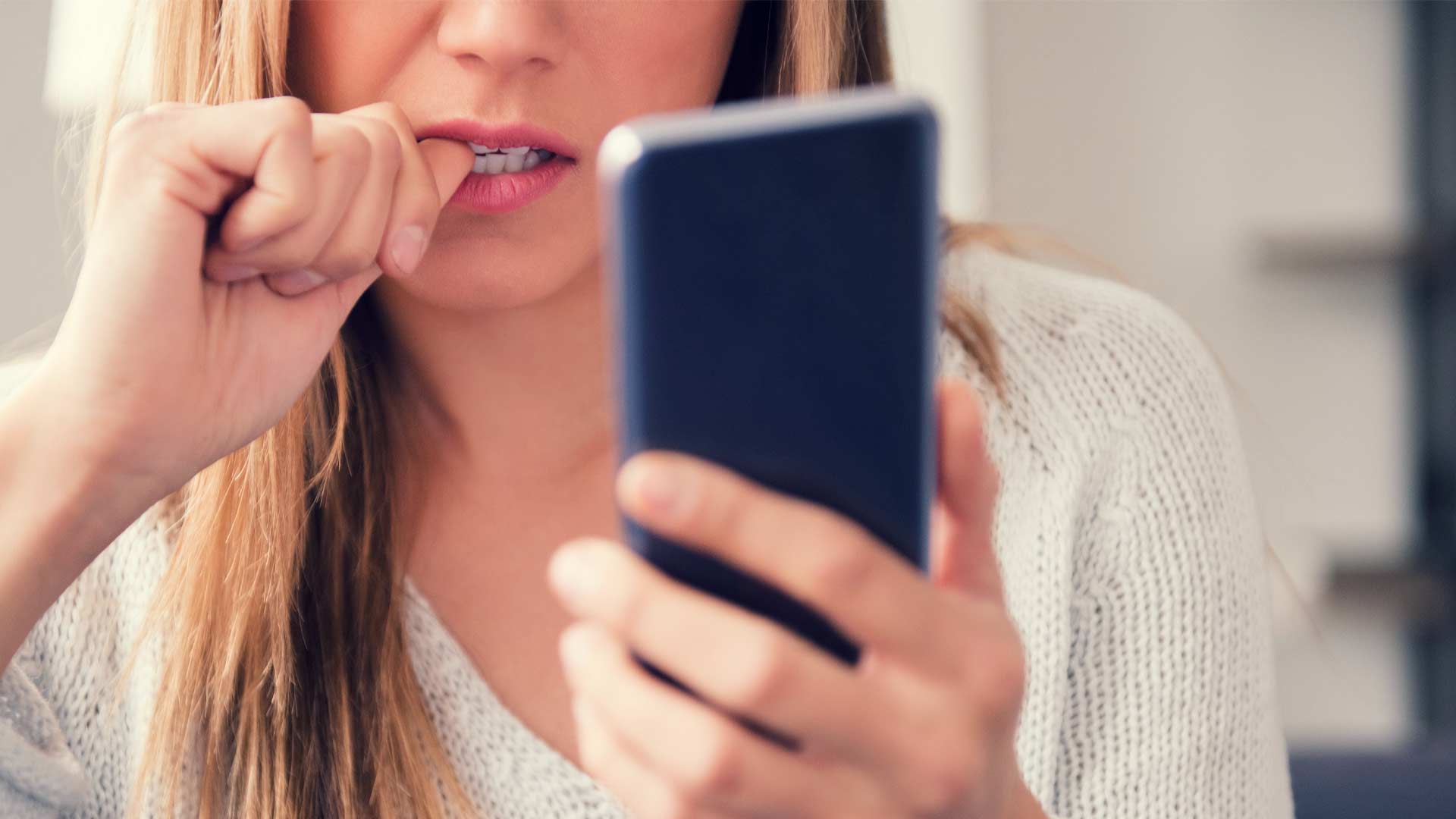 Woman nervously looking at her phone waiting to hear back from a job application.