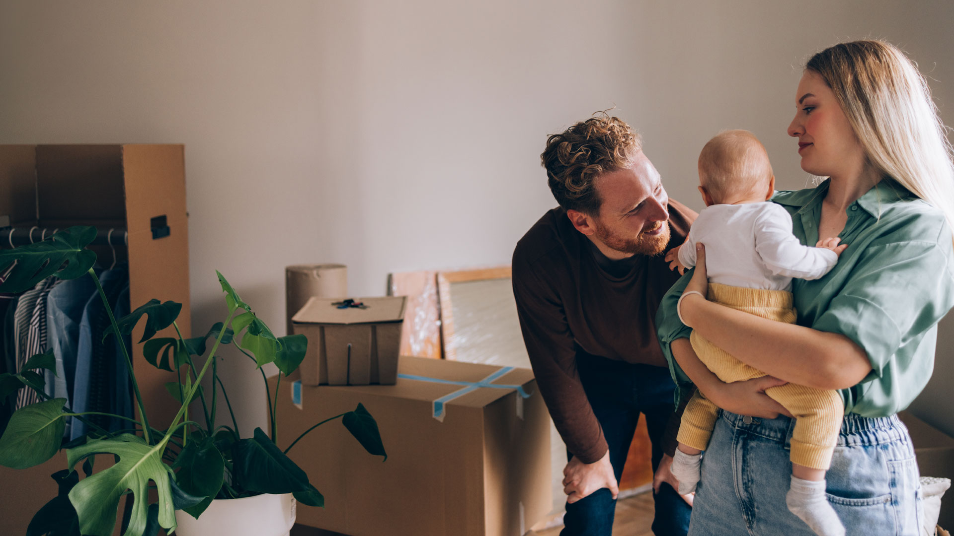 Young family with a baby moving into a rental property, with packing boxes all around them.