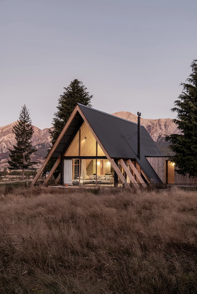 Exposed rafters give the cabin a sense of grounding; macrocarpa weatherboards meet a dark Colorsteel that recesses the east and west elevations into the natural landscape