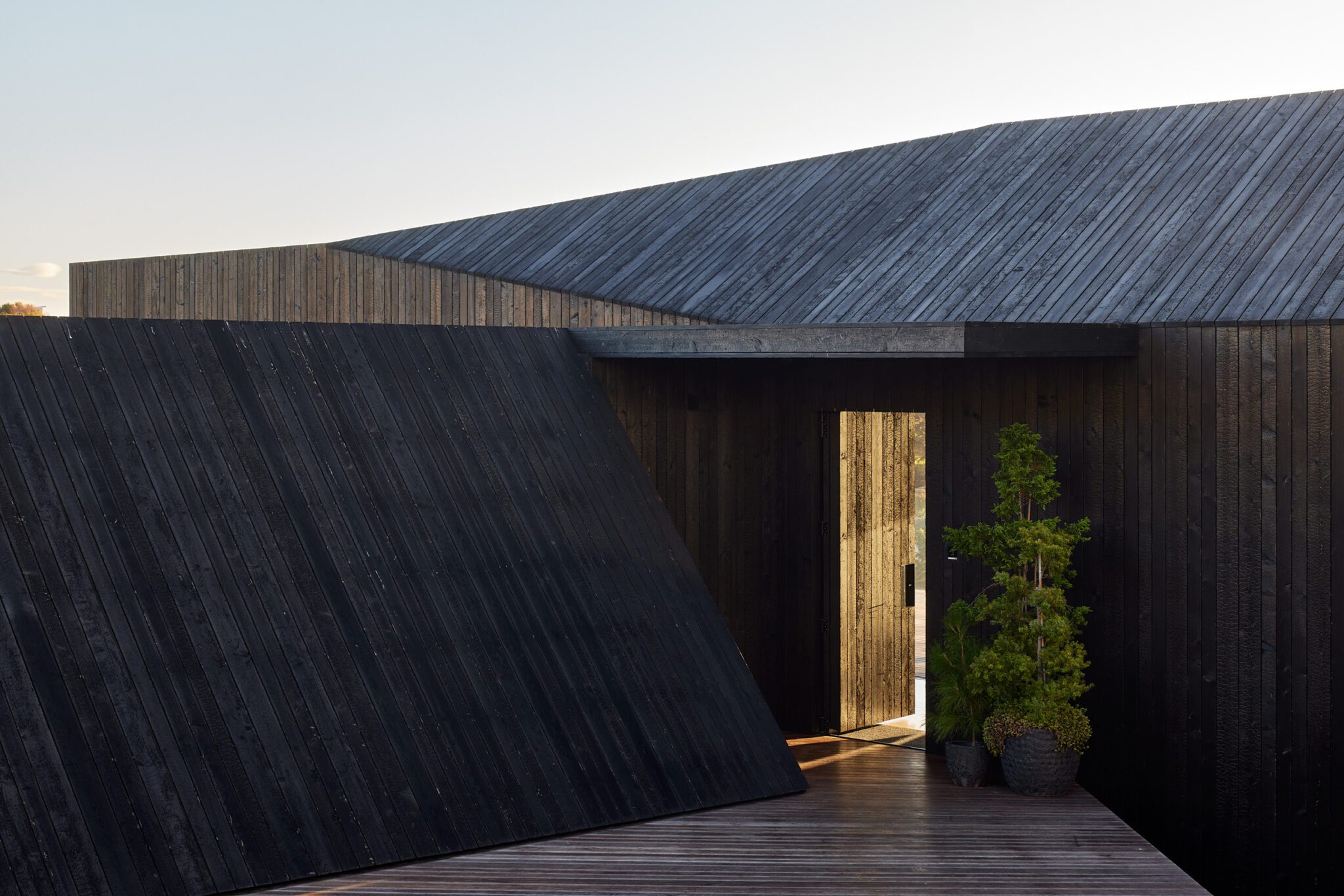 A dark wooden modern building with a hidden door that is slightly open allowing light to seep through