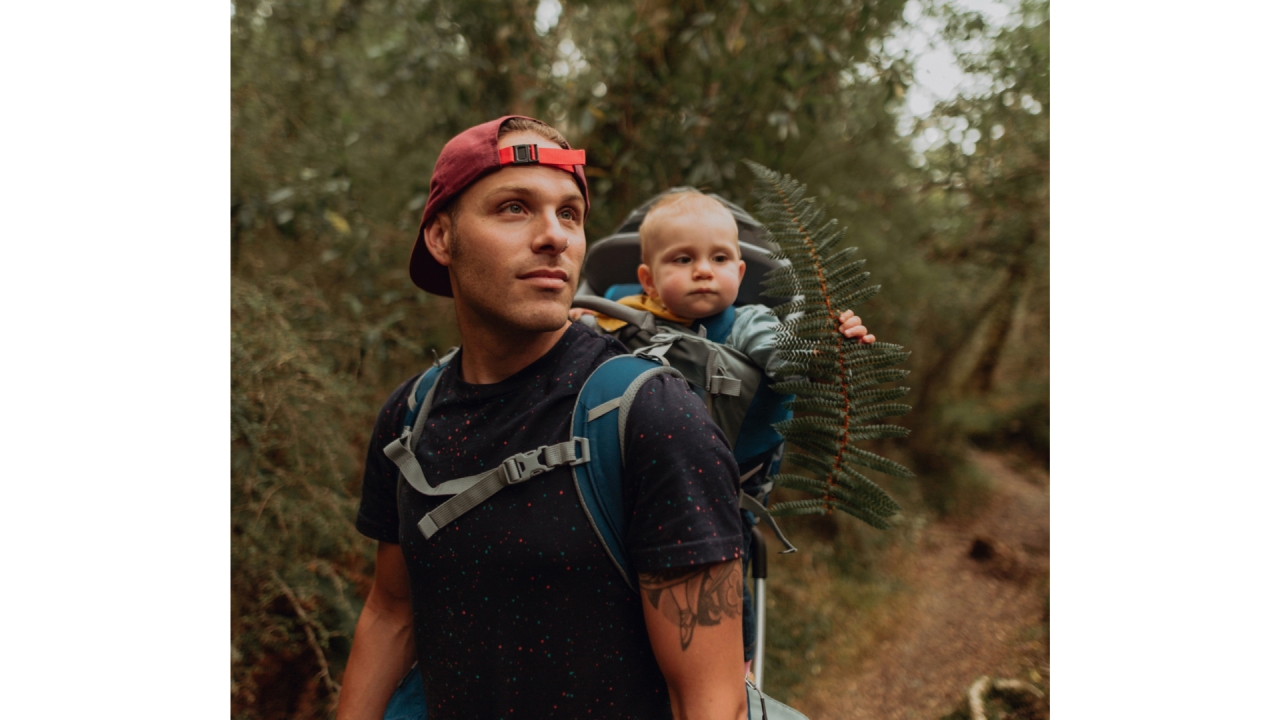 A man hiking in the ngahere (forest) with his baby in a baby carrier on his back.